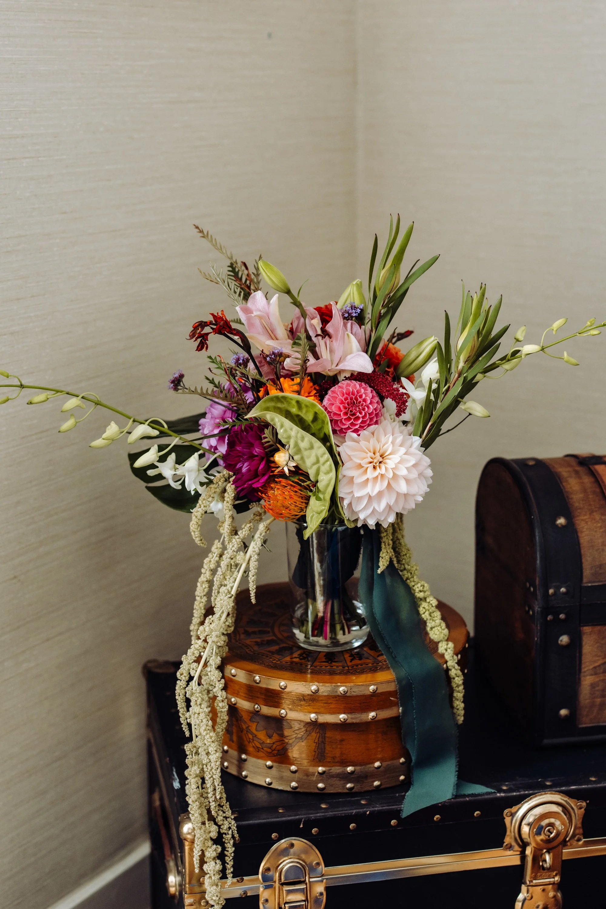Vase of mixed vibrant flowers on a wooden jewelry box beside a vintage trunk.