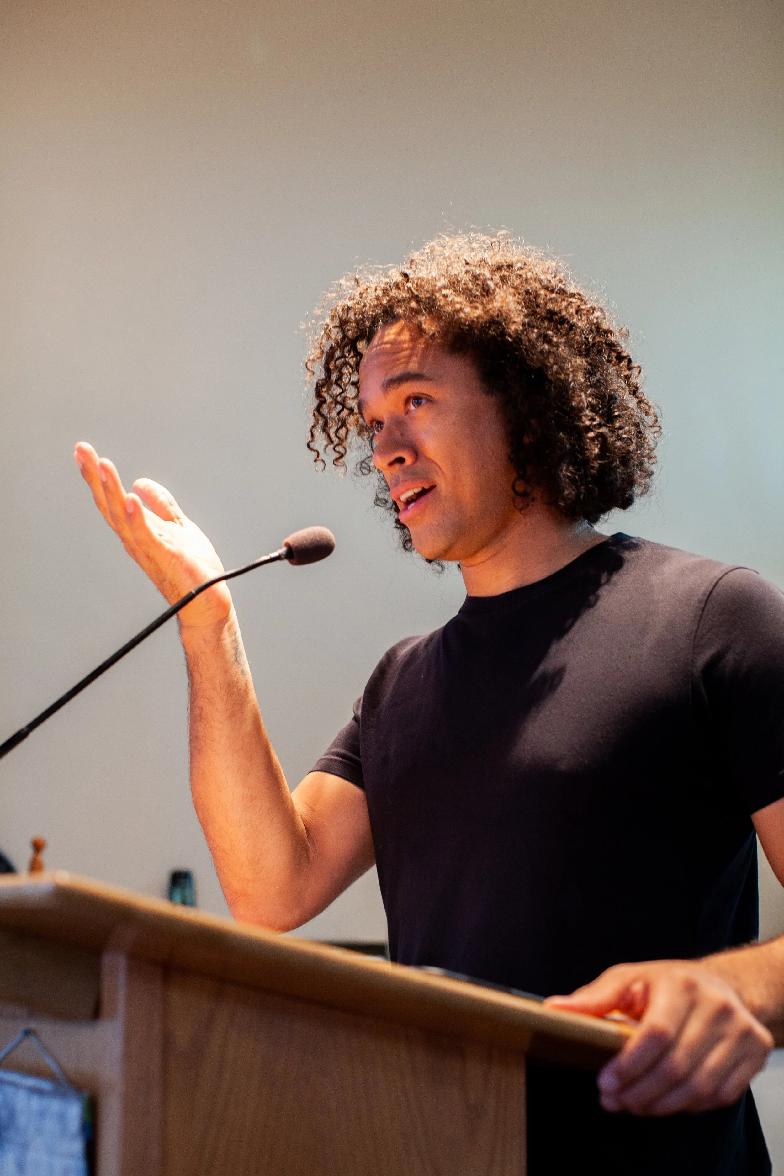 A man with curly hair speaking at a podium with a microphone.