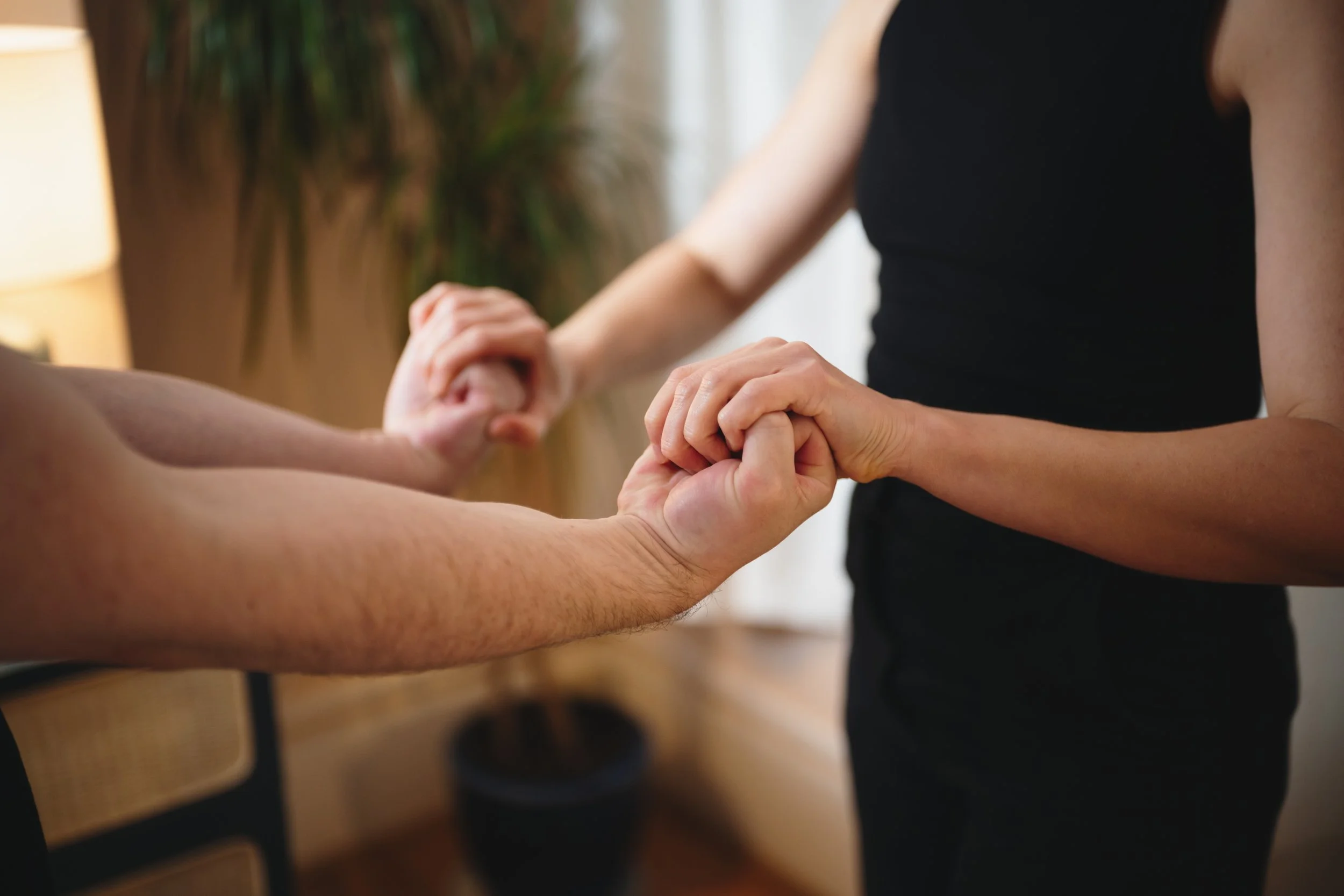 Showing support for patients, working with you to achieve your health goals. Two people holding hands, one with a lighter skin tone and one with a darker skin tone, in a gentle game of hand clasping.