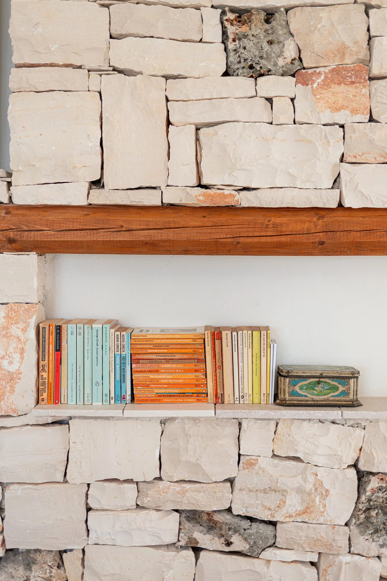 A built-in shelf made of natural stone and wood, with a collection of books and a decorative vintage box, set against a white wall.