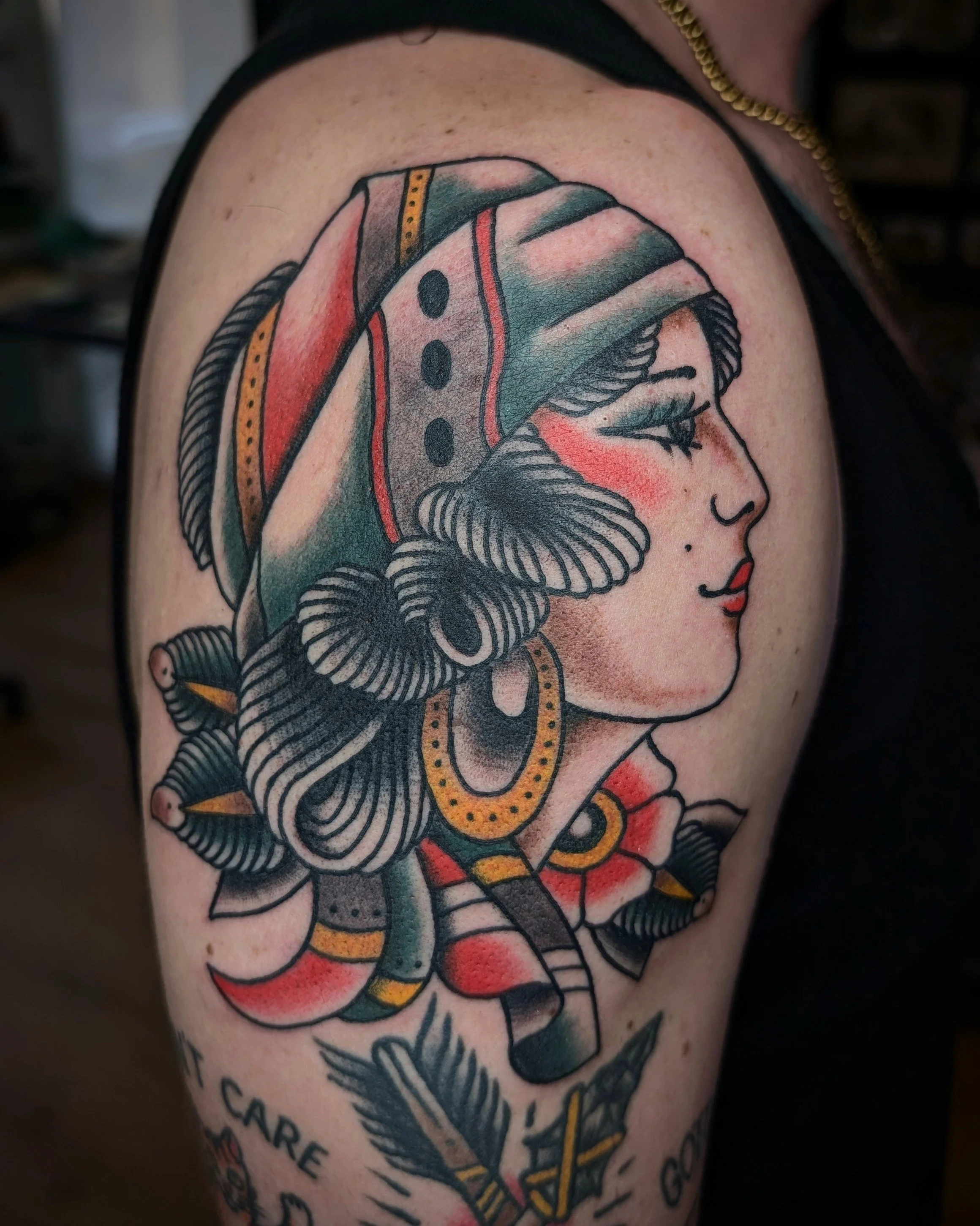 Tattoo eines Porträts einer Frau mit buntem Kopftuch und großen Ohrringen auf dem Oberarm.