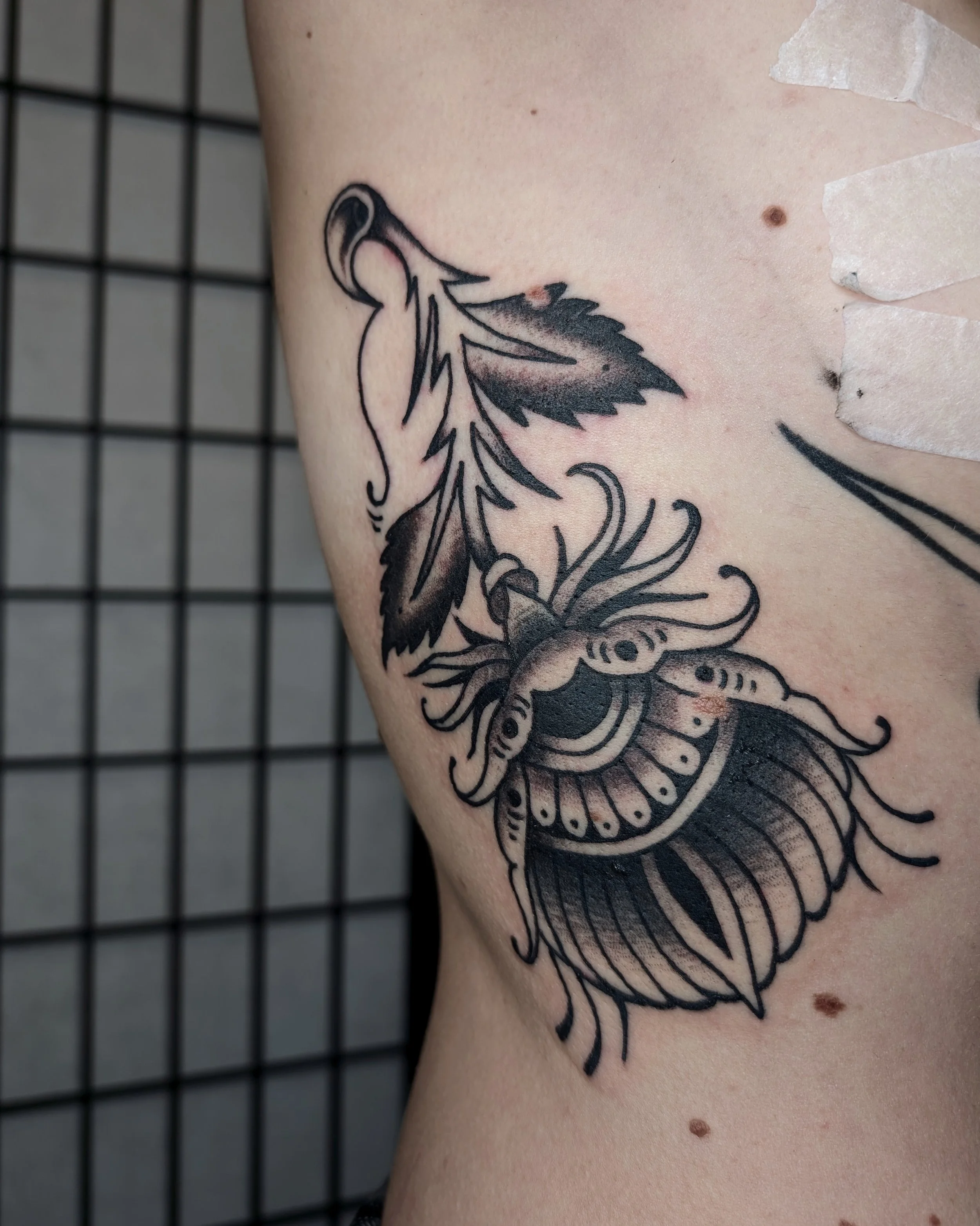 Schwarzes Tattoo eines stilisierten Insekts mit Flügeln auf der Haut