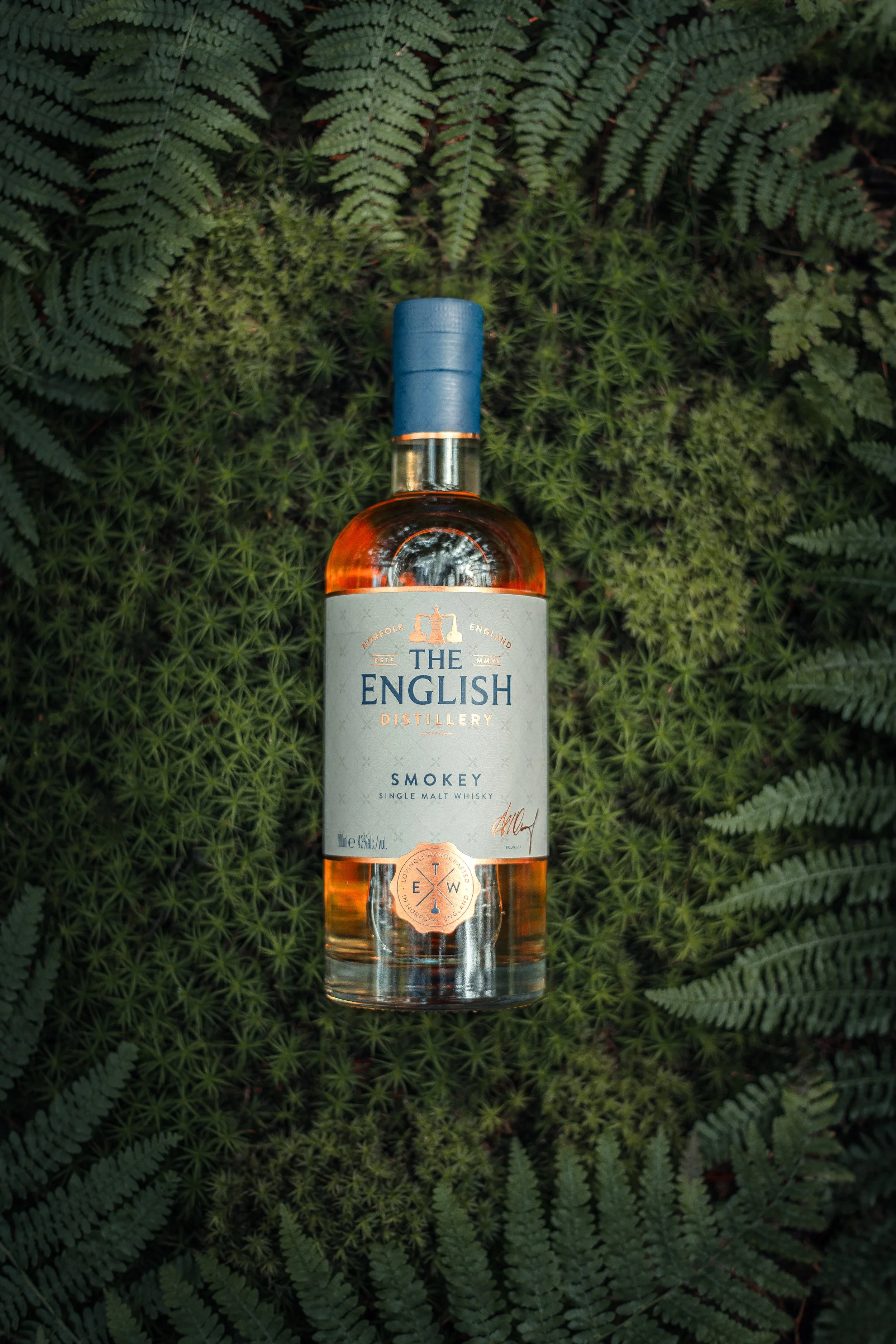 A bottle of The English Distillery Smokey single malt whisky placed on green fern leaves.
