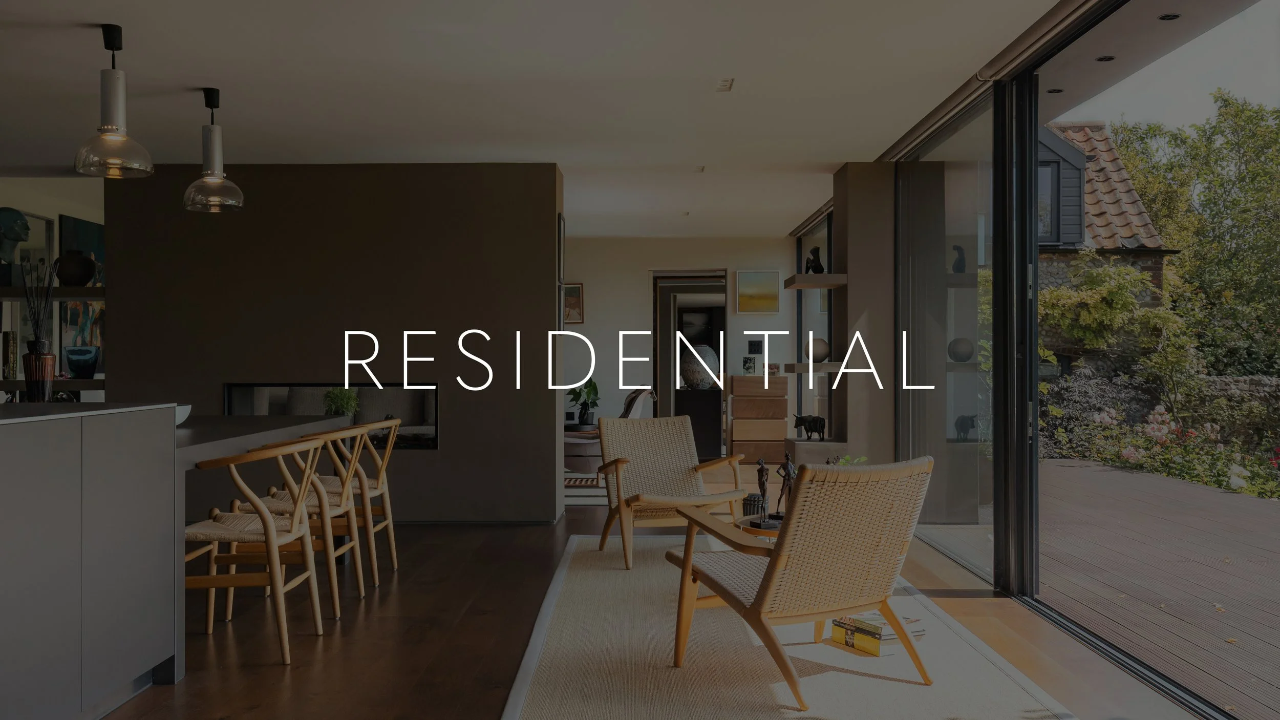 Interior of a modern residential living space with a dining area, chairs, and large sliding glass doors opening to a deck and garden outside.