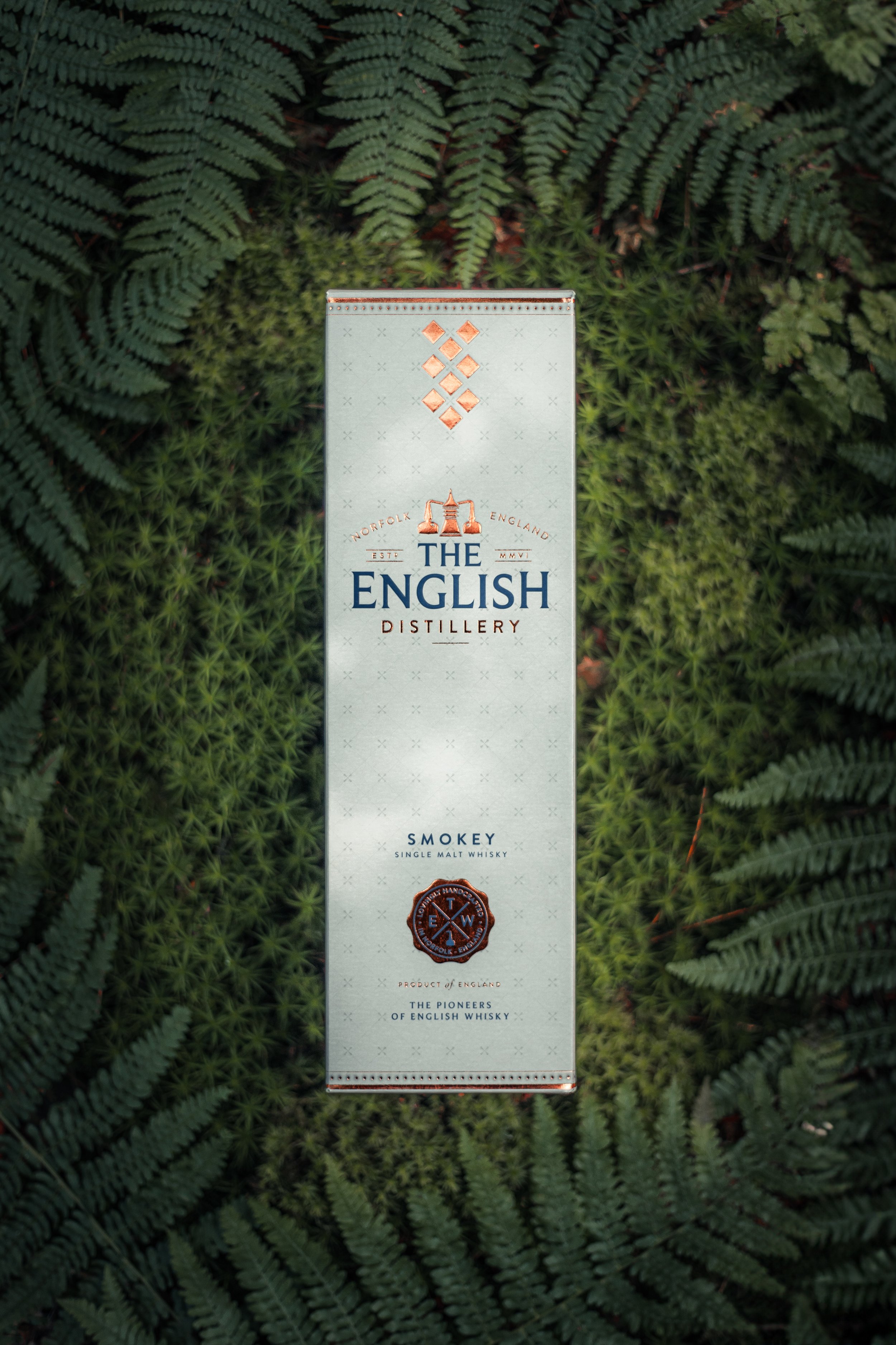 A box of The English Distillery smokey single malt whisky placed on green fern leaves.