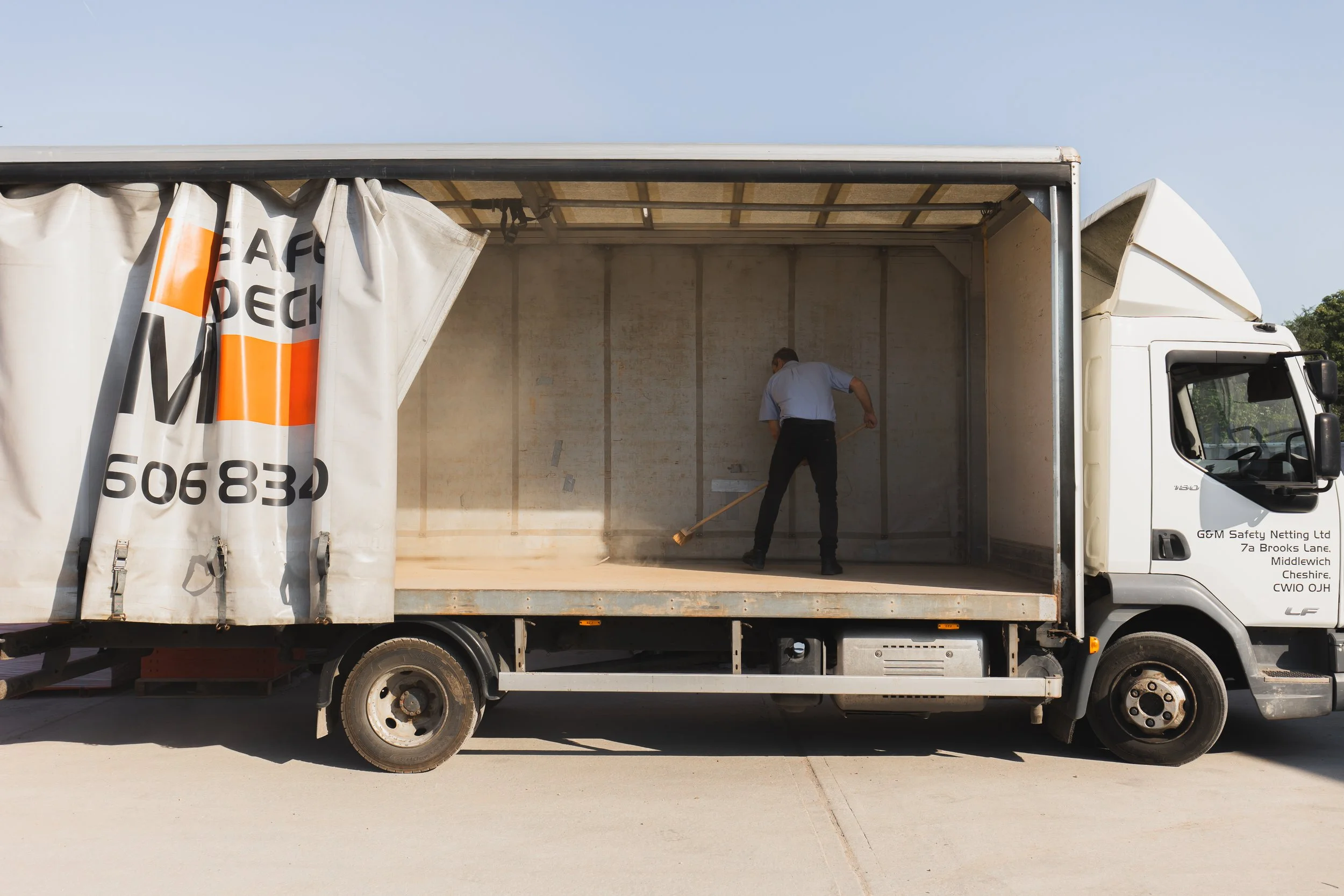 A man cleaning the empty inside of an open truck with a broom during daytime.