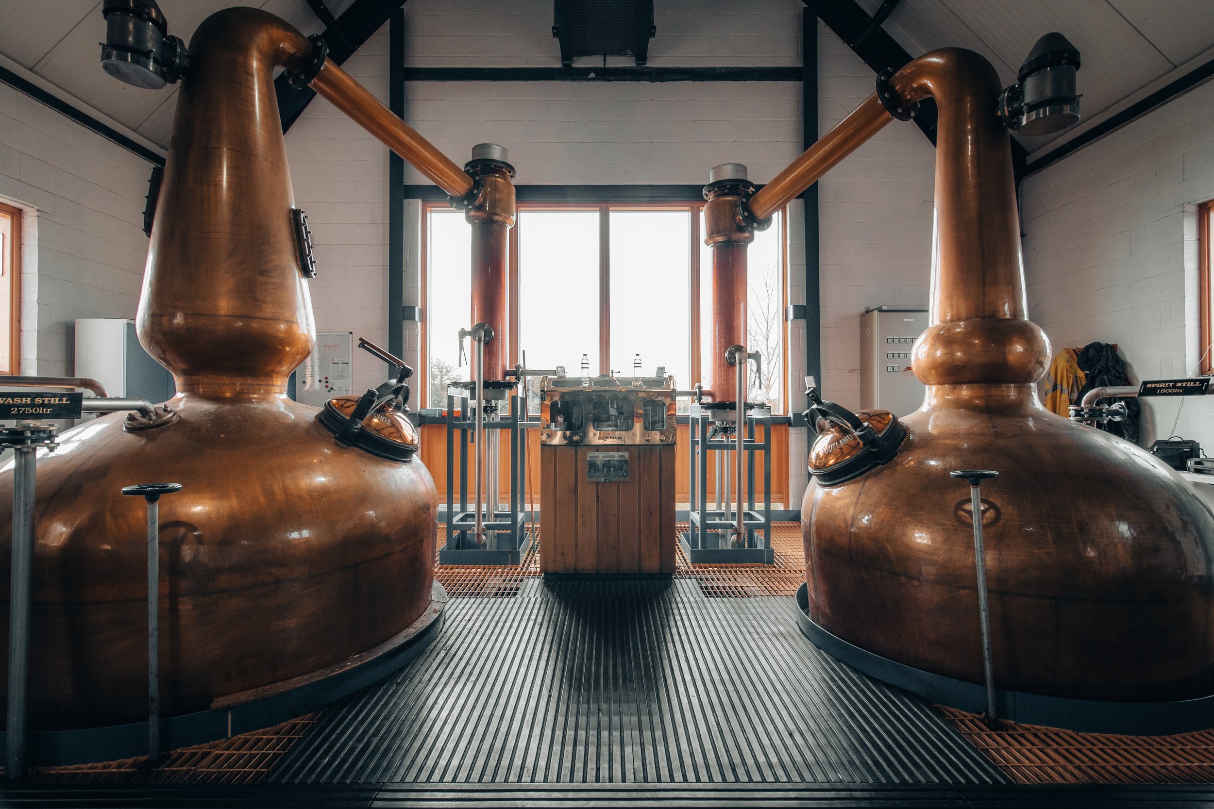 Large copper distillation tanks in a distillery with a window in the background.