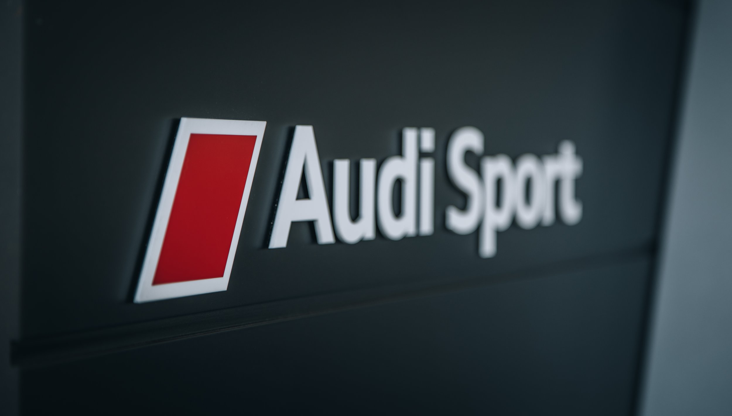 Close-up of the Audi Sport logo on a dark background.