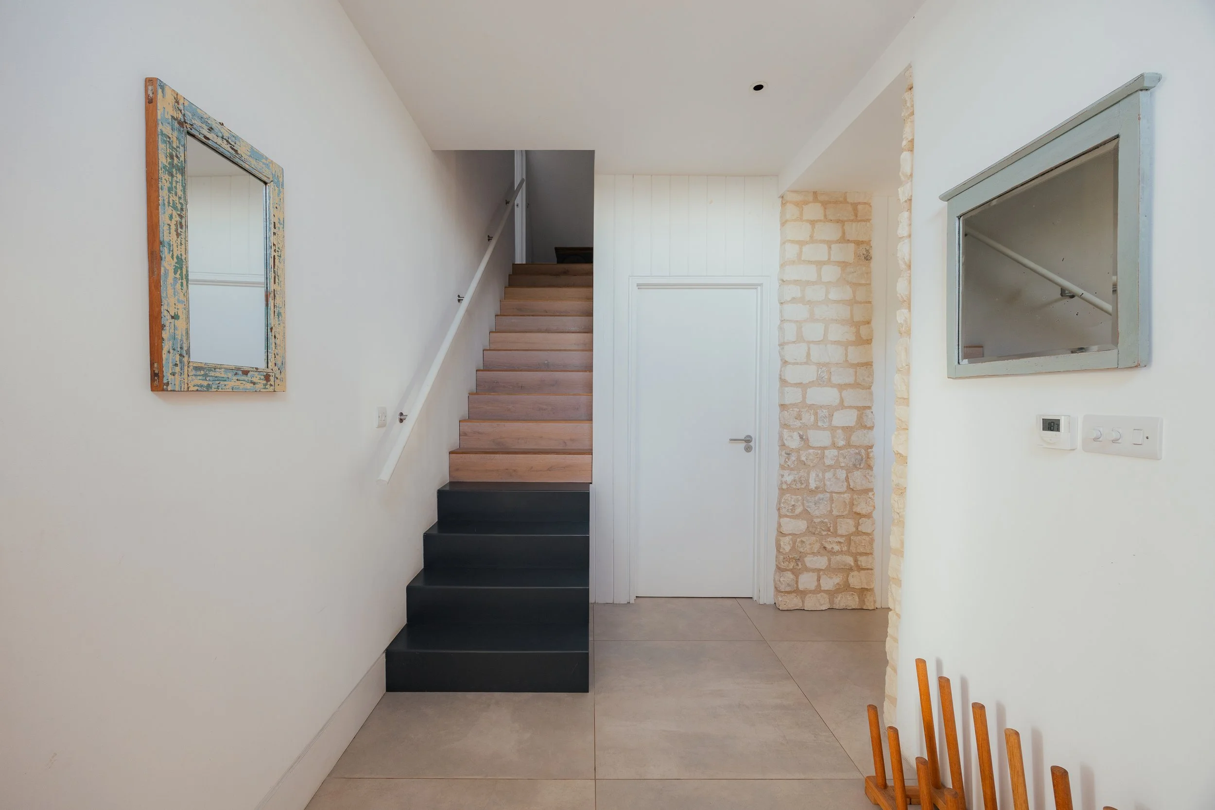 Interior view of a modern house with a staircase, white walls, a brick column, and a mirror on the wall.