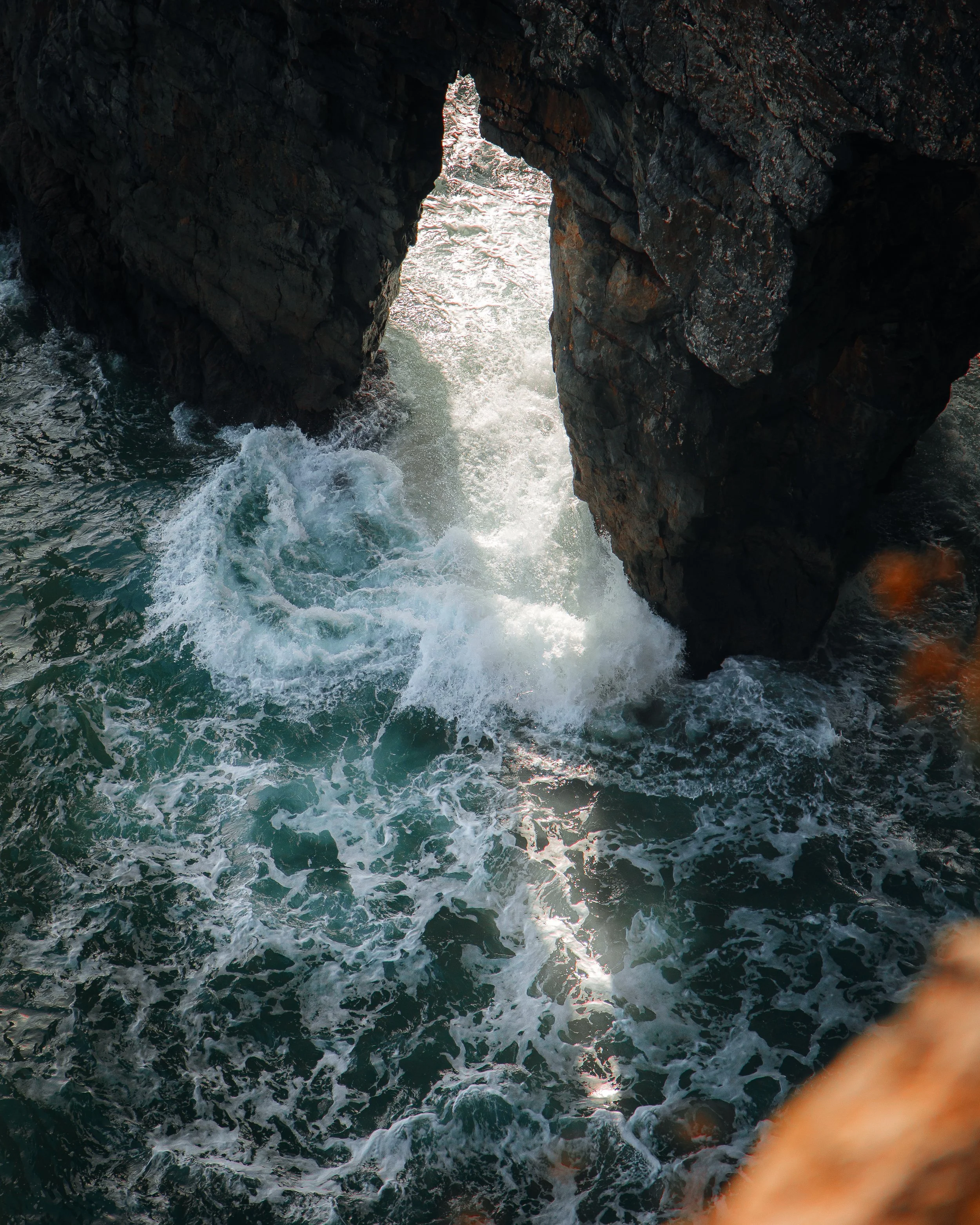 Ocean waves crashing through a large natural rock arch in the sea.