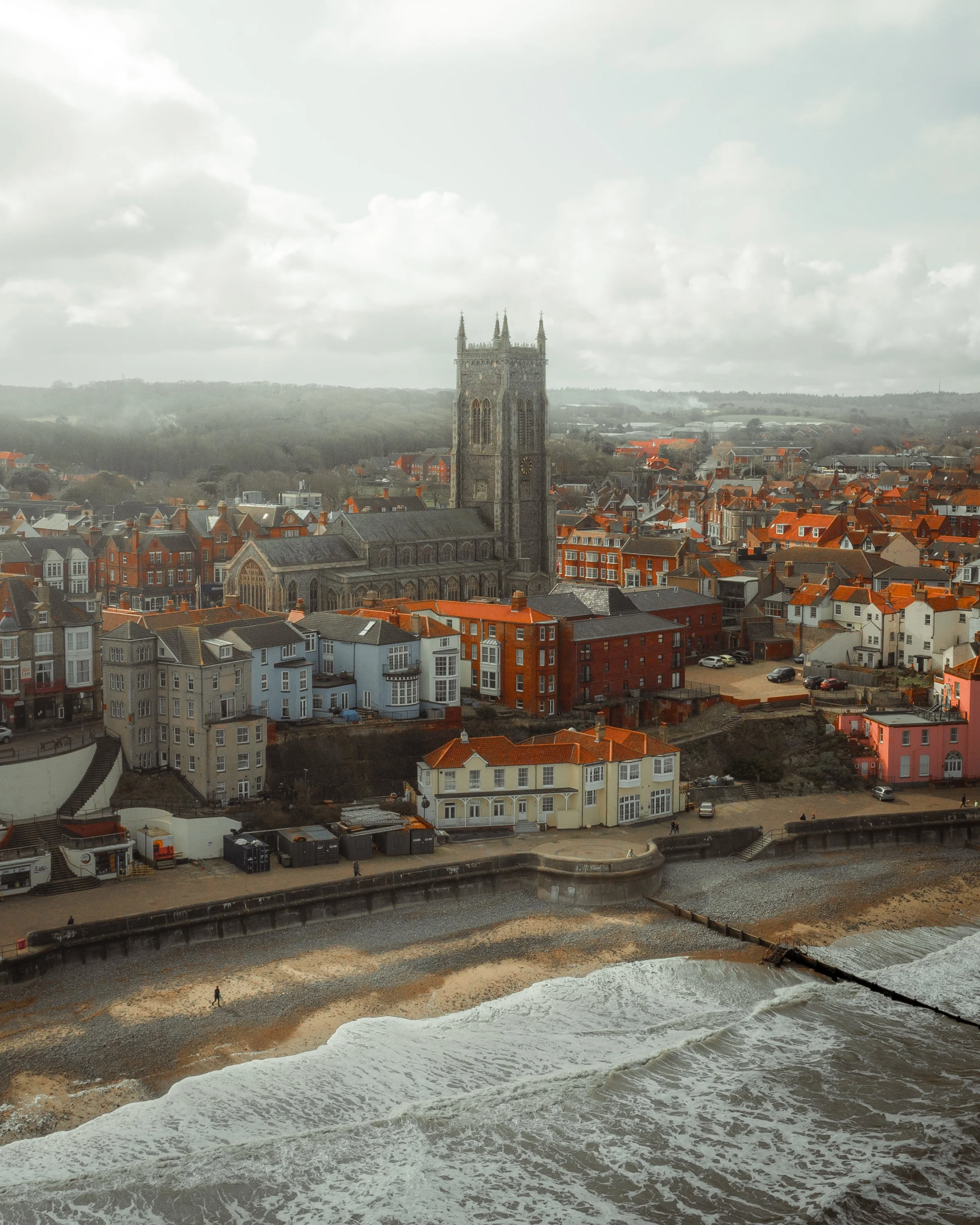 Coastal town with colorful houses, a church with a tall steeple, and the ocean in the foreground.