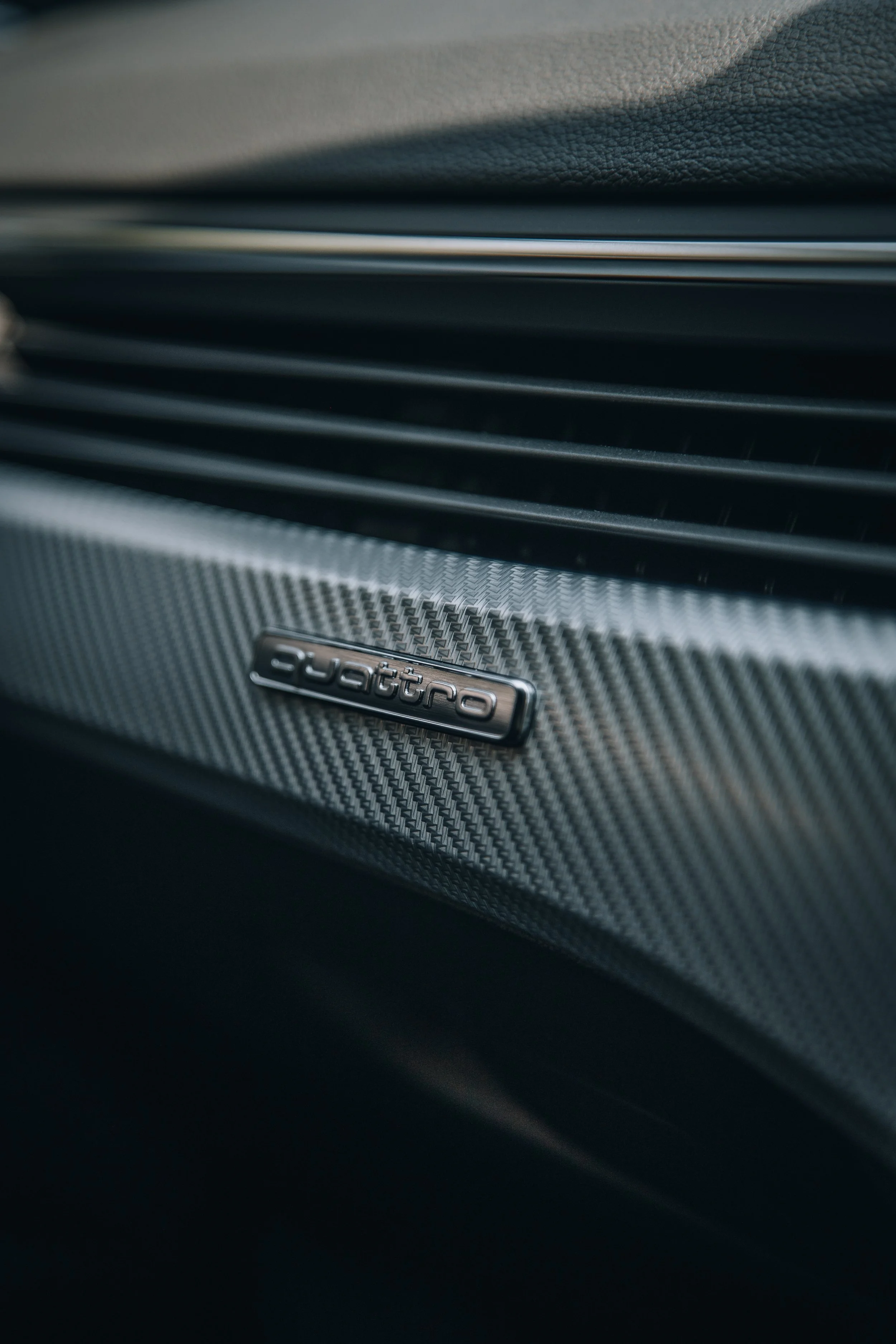 Close-up of a carbon fiber panel with an Audi logo.