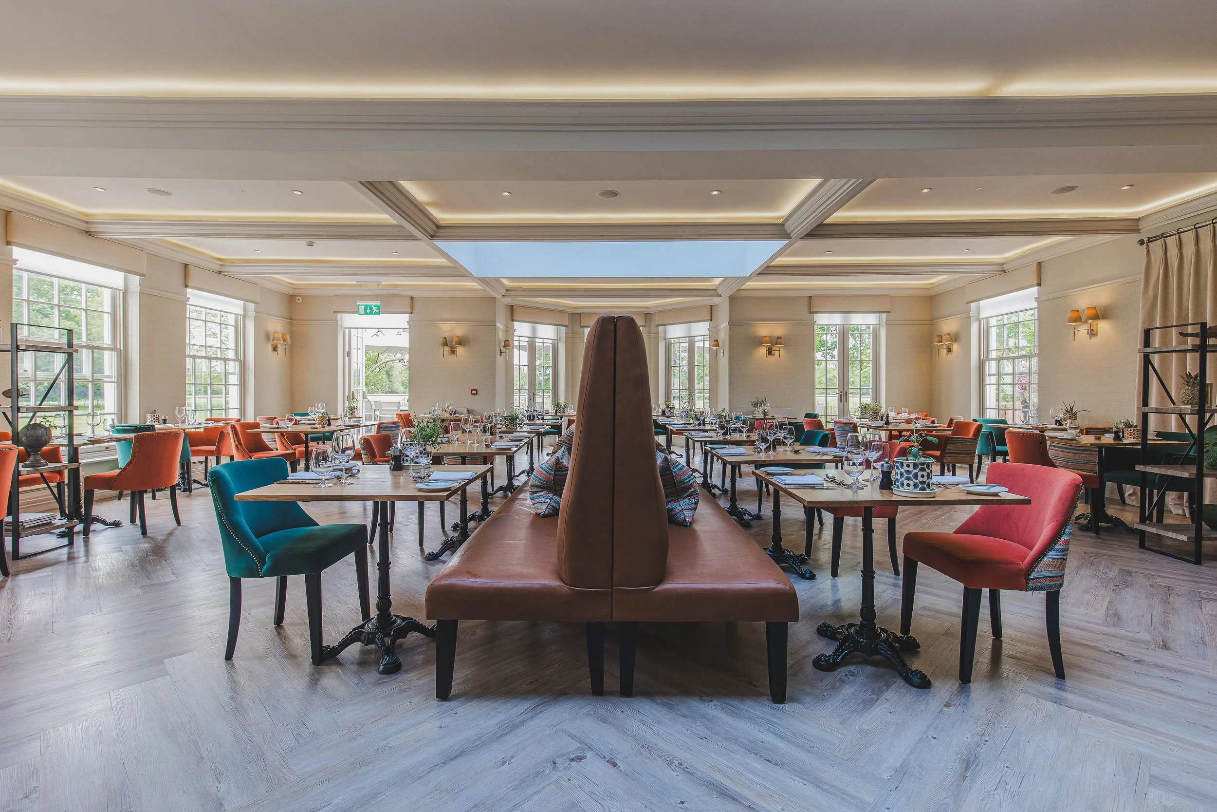 A spacious restaurant dining area with multiple tables set for a meal, surrounded by colorful chairs and large windows letting in natural light.