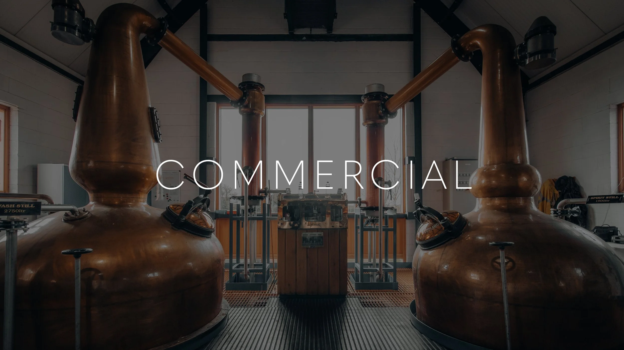Interior view of a distillery with large copper stills and distillation equipment, labeled as 'commercial'.