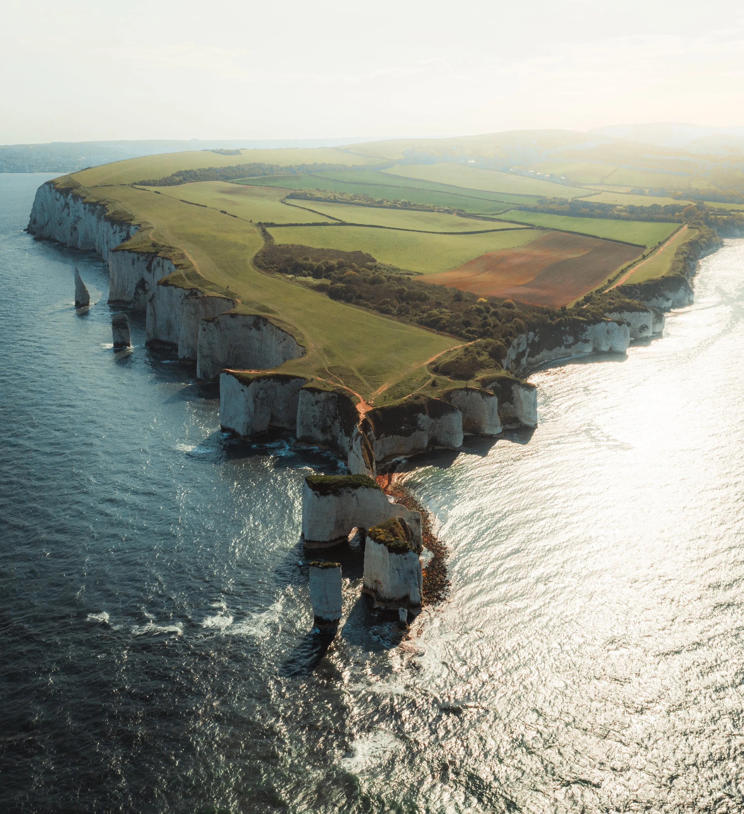 Aerial view of white chalk cliffs along the coastline with green fields and a sailboat in the water.