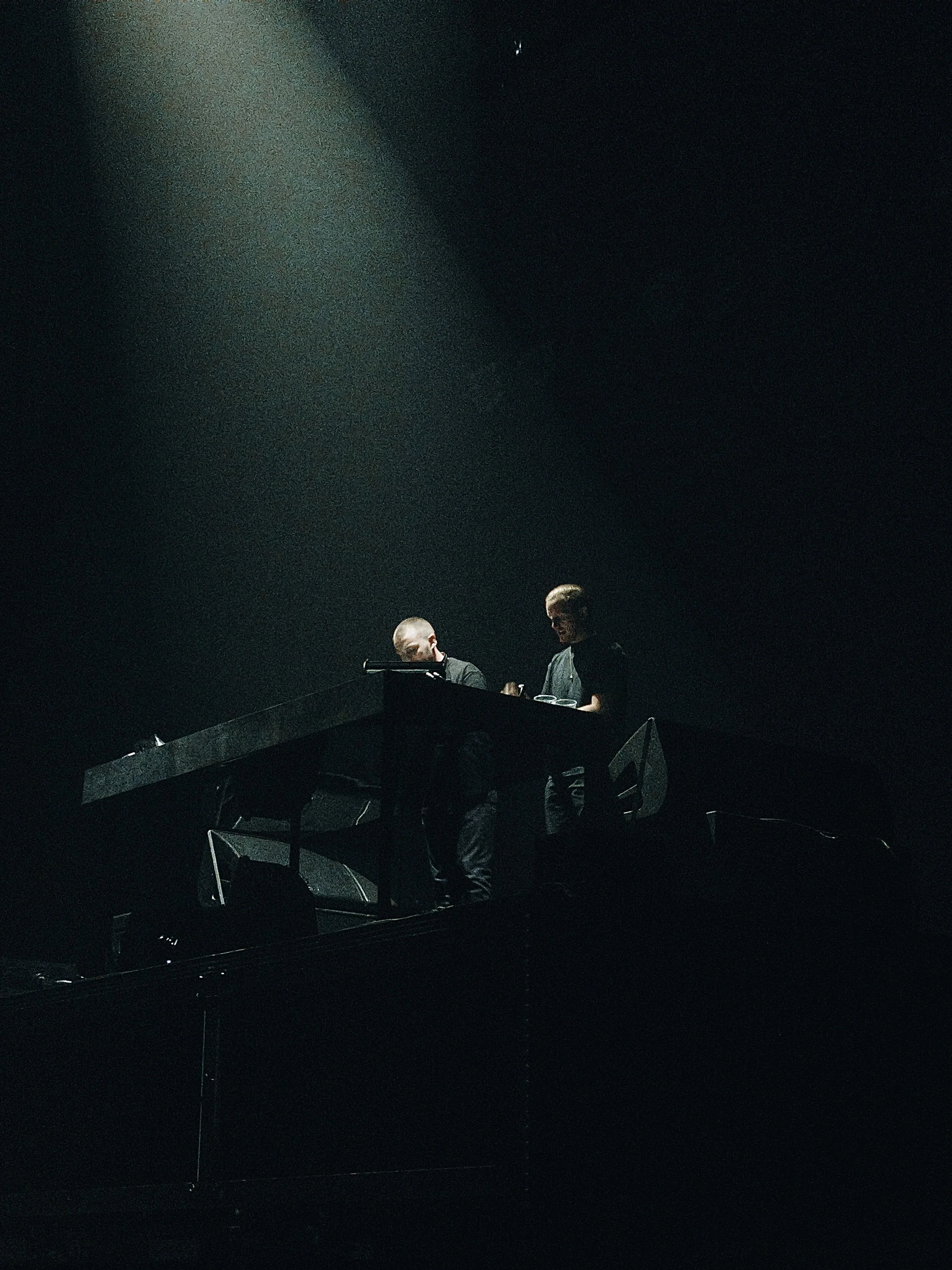 Two people performing on a dark stage at a concert, illuminated by a spotlight.