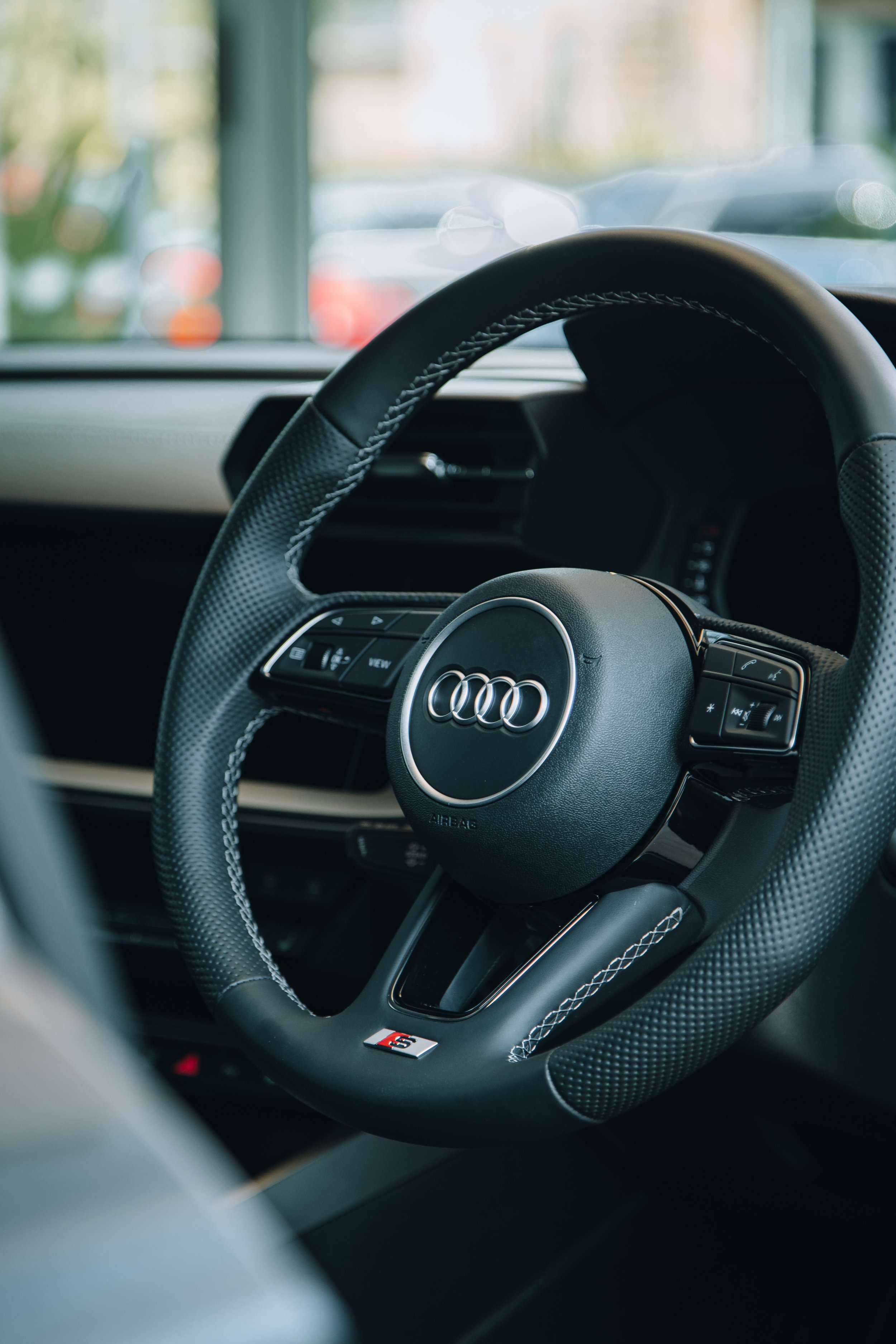 Close-up of an Audi car steering wheel with the Audi logo and an 'S' badge inside the vehicle.