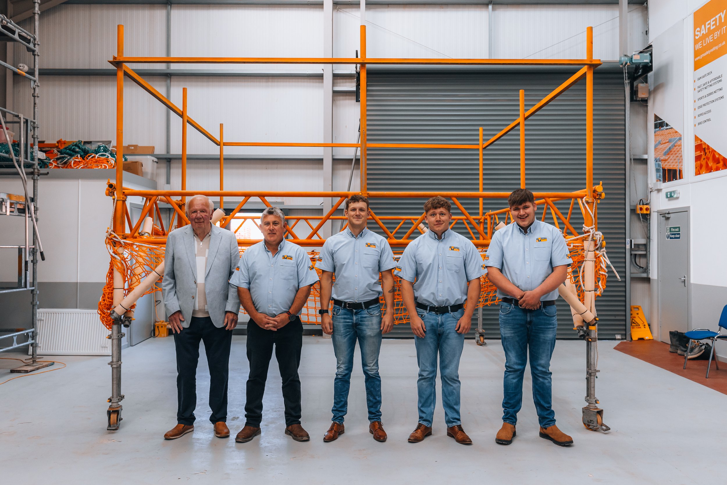 Group of five men standing in front of an orange scaffolding structure inside a warehouse.