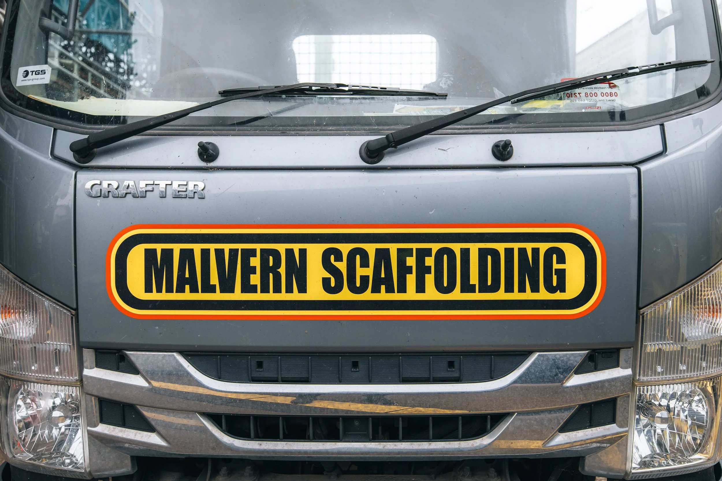 Close-up of the front of a gray GRAFER truck with a large yellow and black sticker that reads MALVERN SCAFFOLDING.