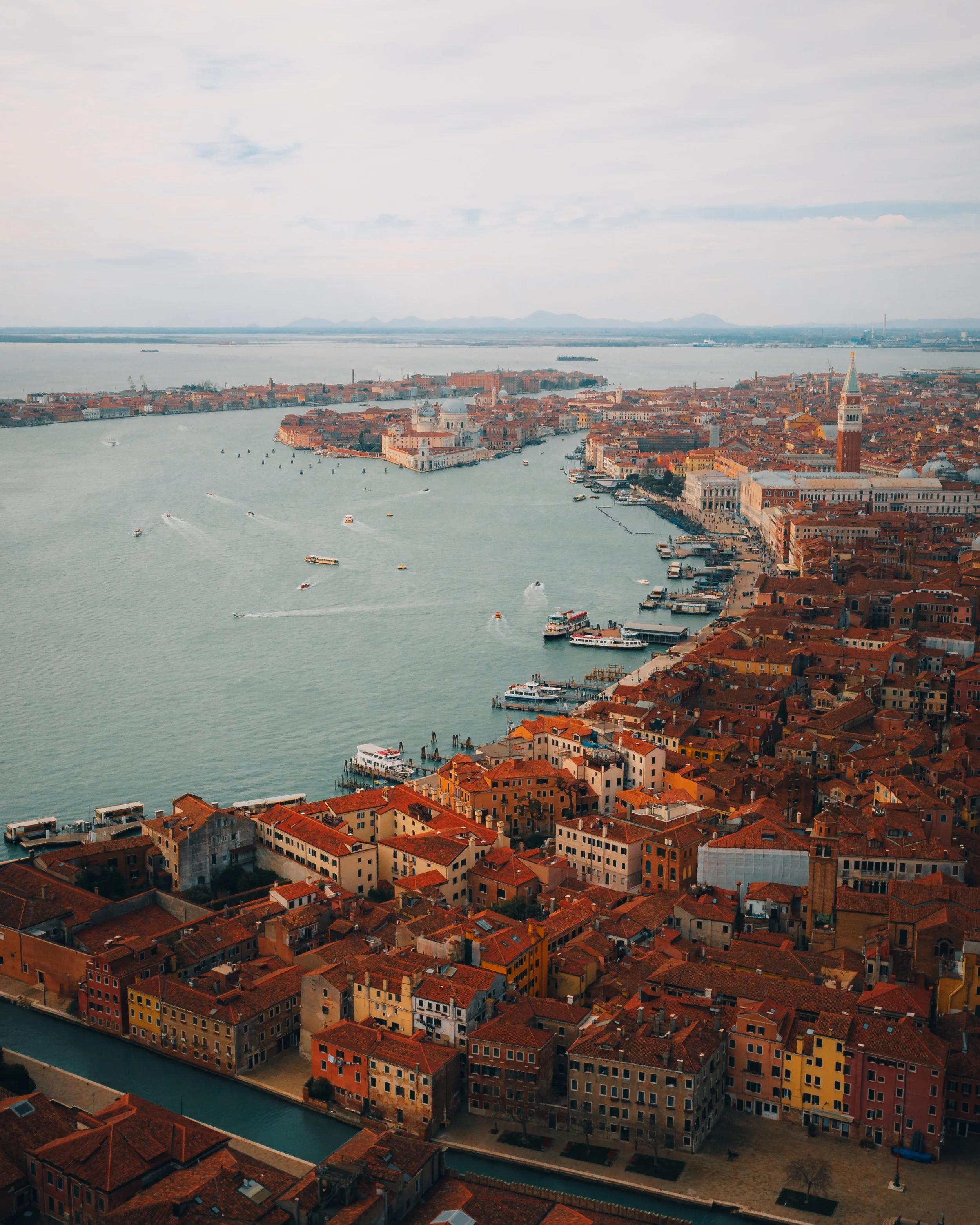 Aerial view of Venice, Italy, showing canals, boats, and historic buildings with red-tiled roofs.