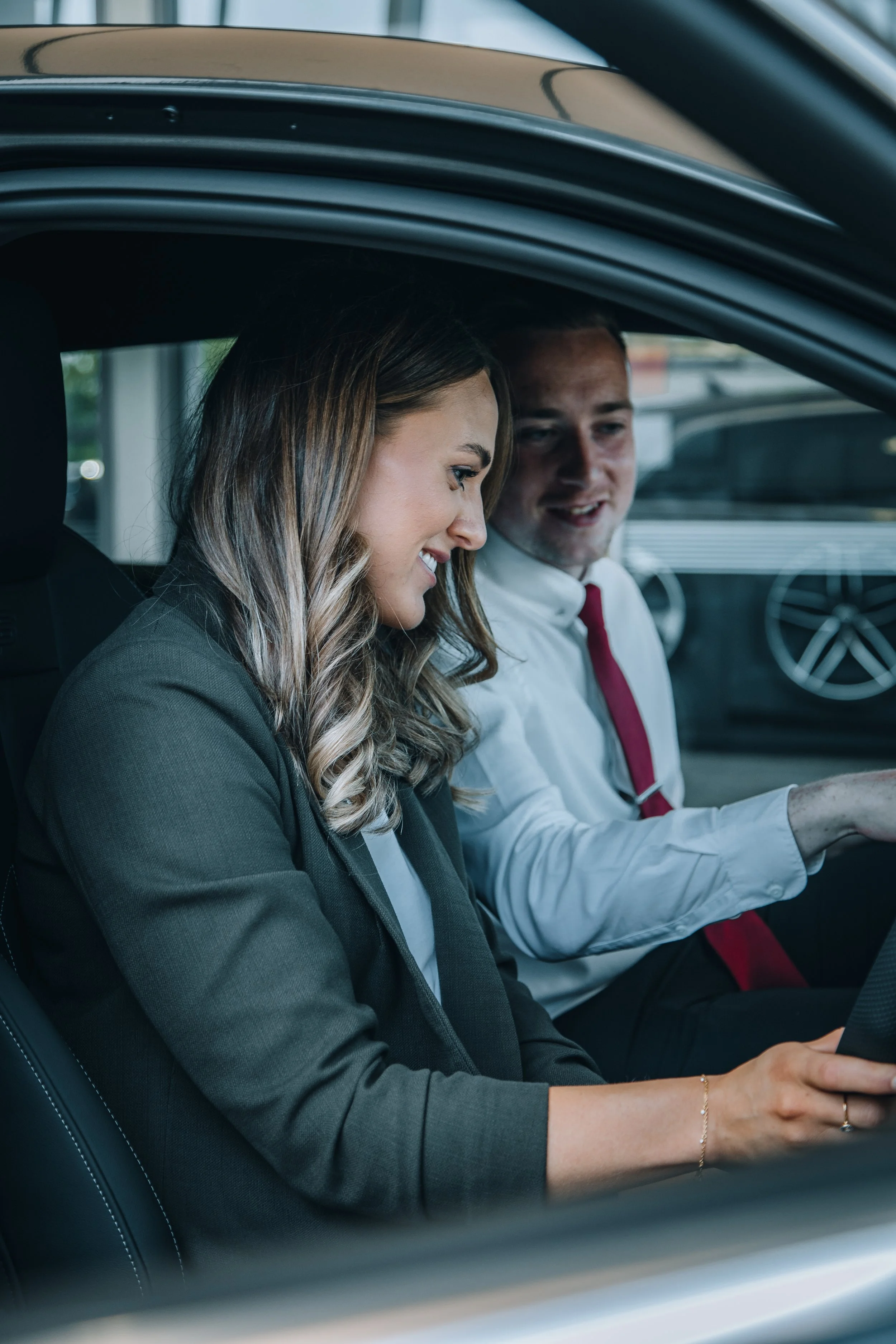 A woman and a man sitting in a car, looking at a device or screen with smiles.