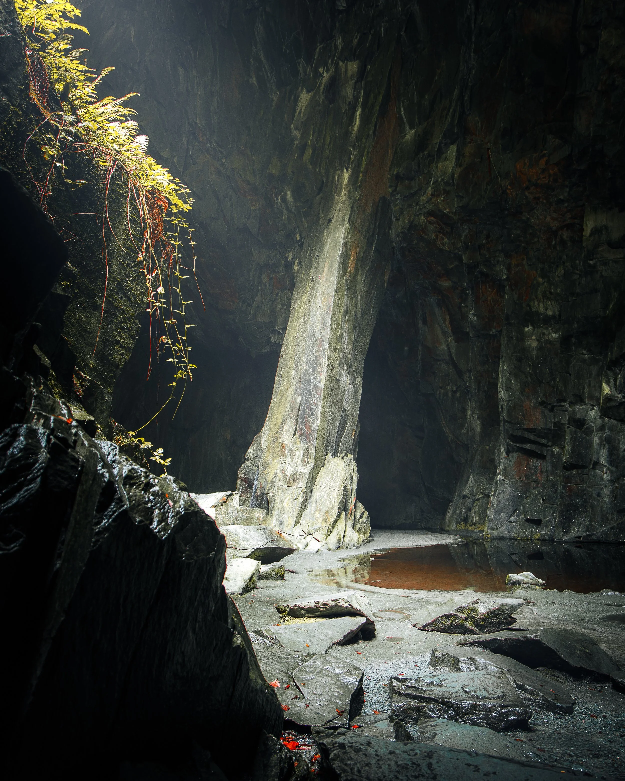 A dark cave with a large rocky formation and a small pool of water on the floor.