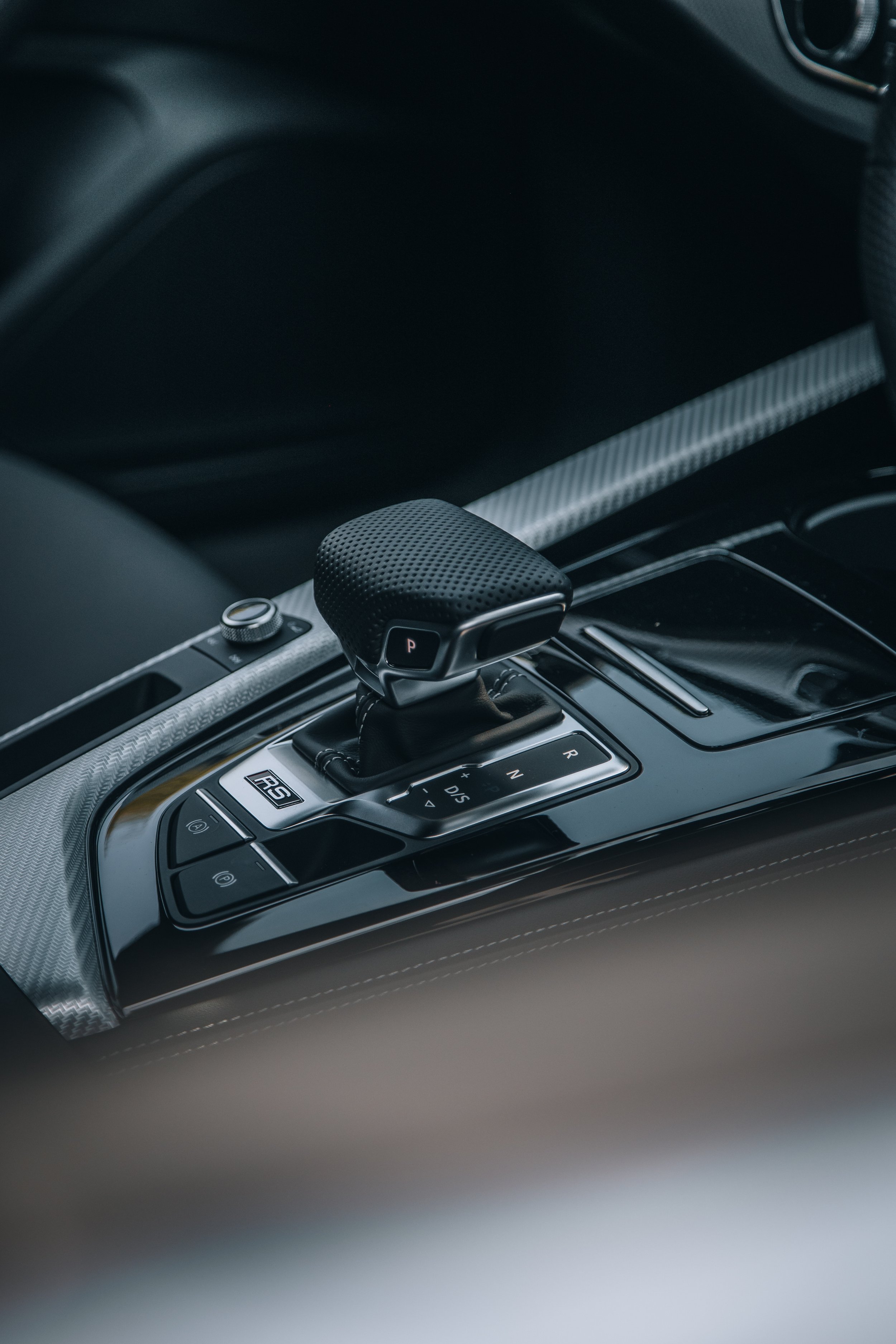 Close-up of a gear shift lever in a sports car, with various driving mode buttons and a modern interior.
