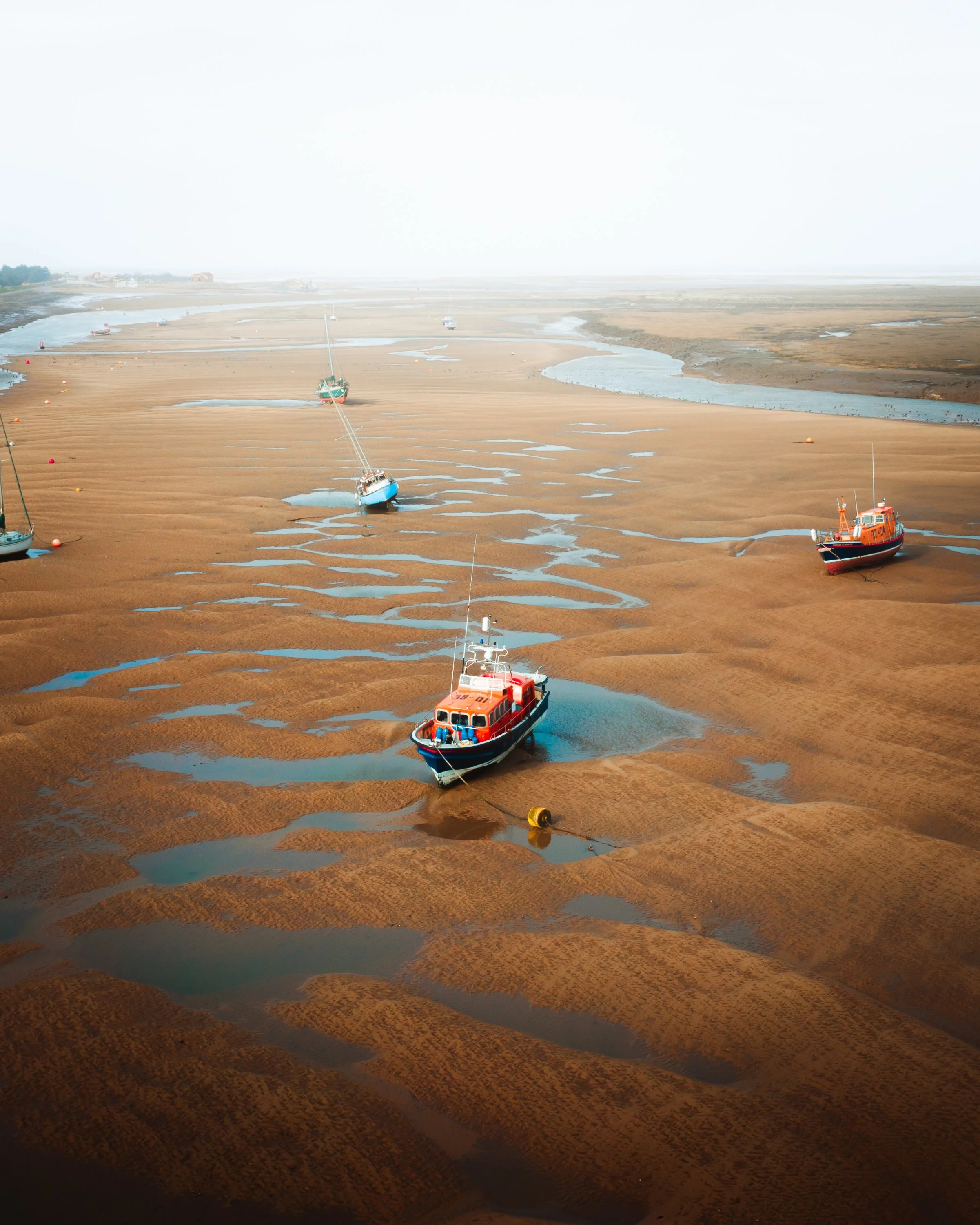 Boats stranded on a low tide sandy beach with water pools and mud flats.