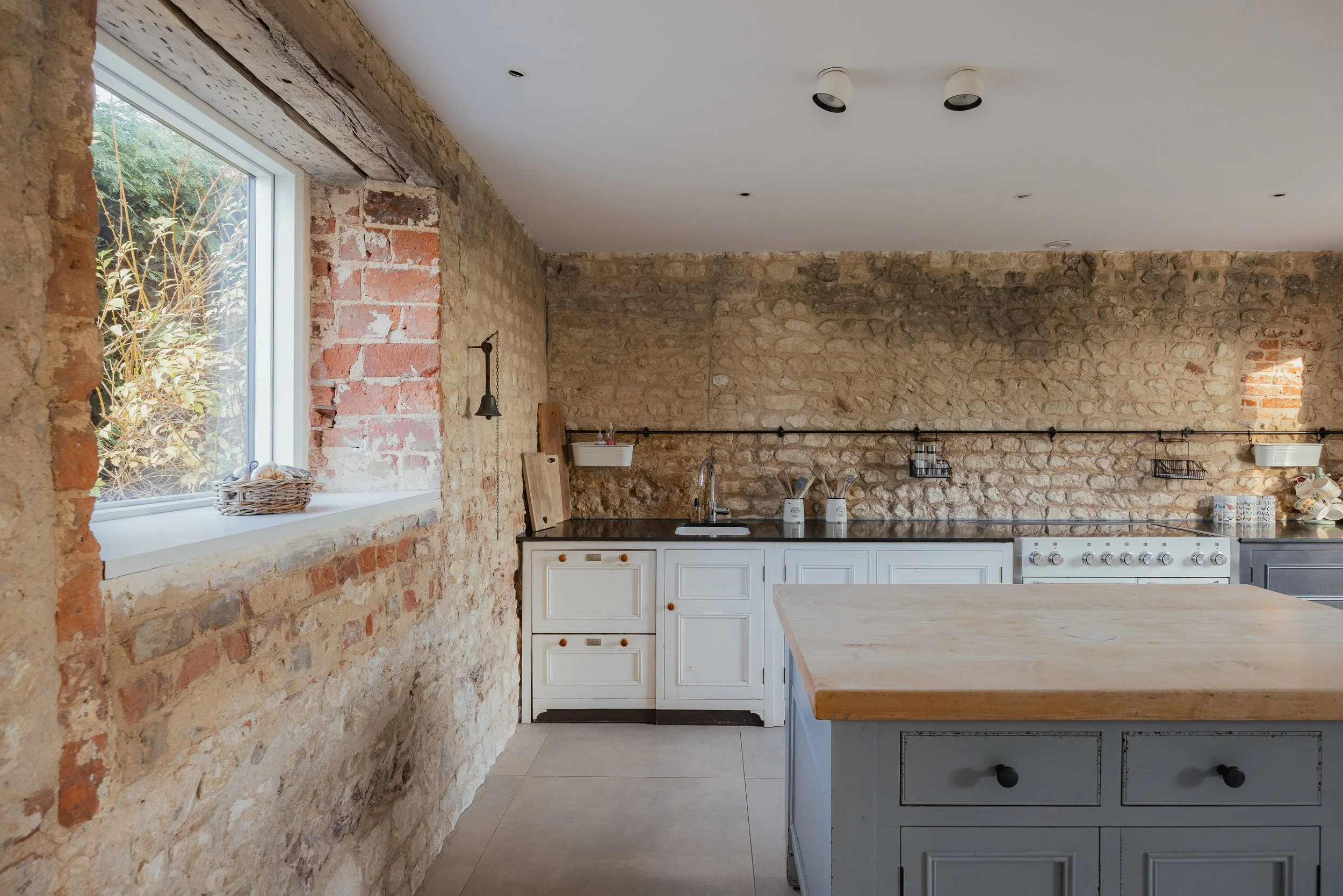 Kitchen with exposed brick walls, white cabinets, a wooden island, and a window with outdoor view.