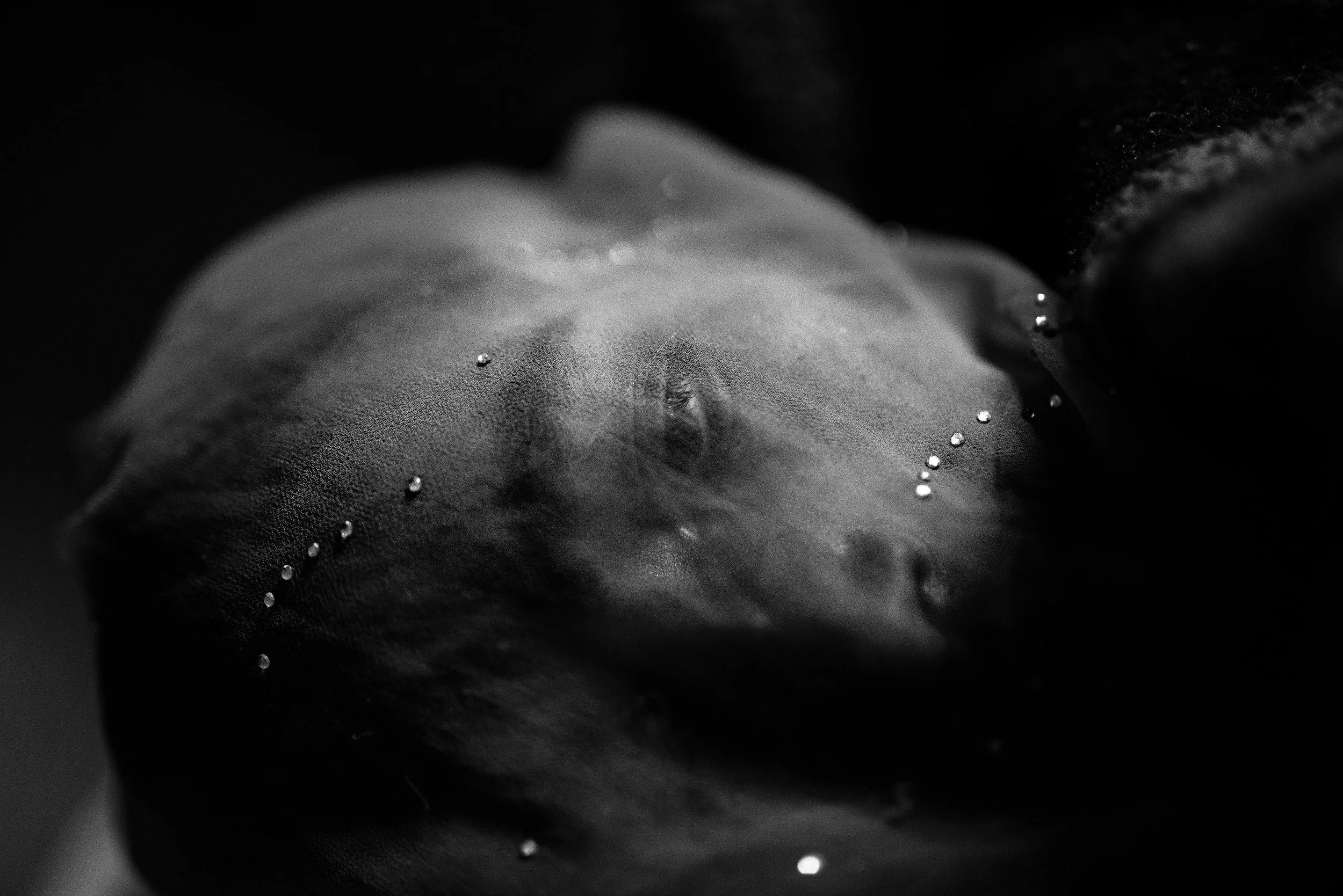 Una mujer dormida debajo de una telaraña con gotas de agua, en blanco y negro.