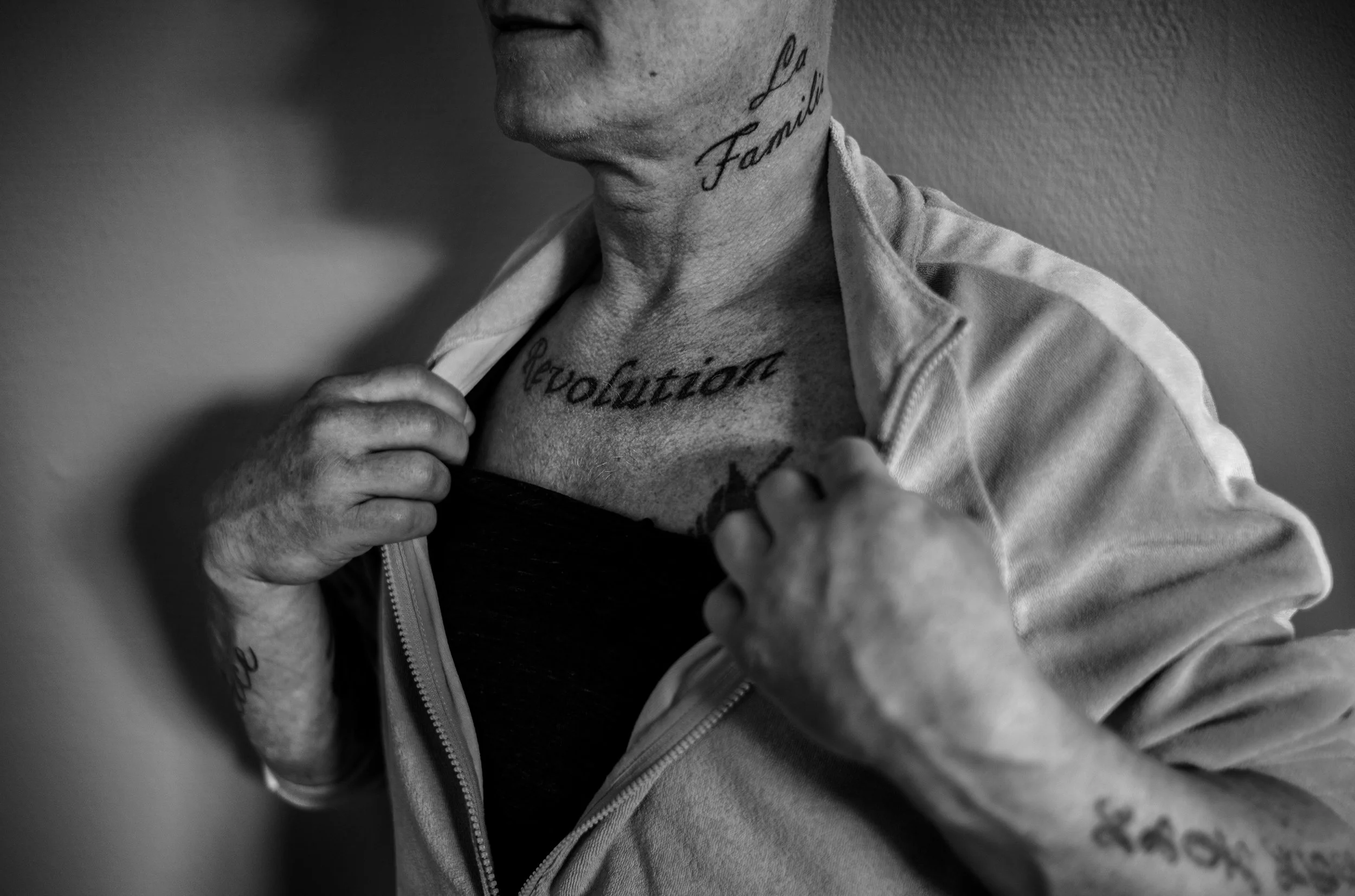 Persona masculina con tatuajes en el cuello, pecho y brazos, levantando la camisa para mostrar las marcas.