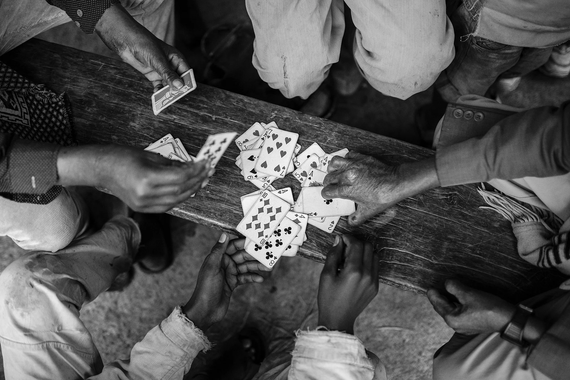 Manos de varias personas jugando a las cartas sobre una mesa de madera