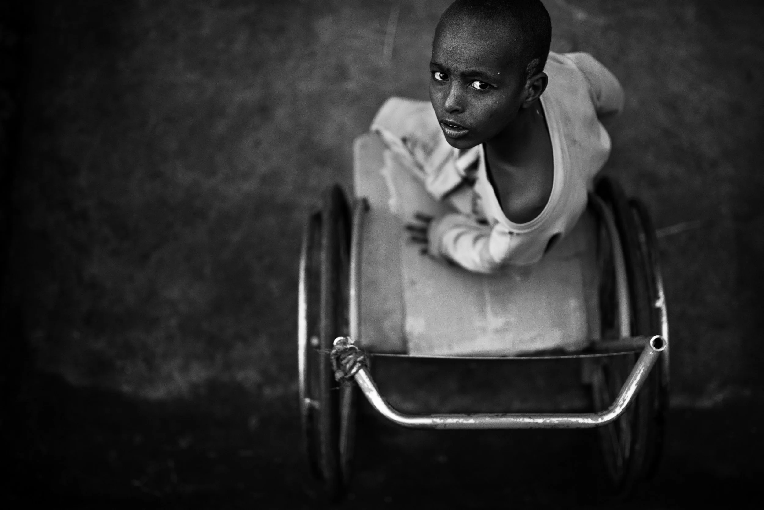 Niño en silla de ruedas, mirando hacia arriba, en un entorno oscuro en blanco y negro.