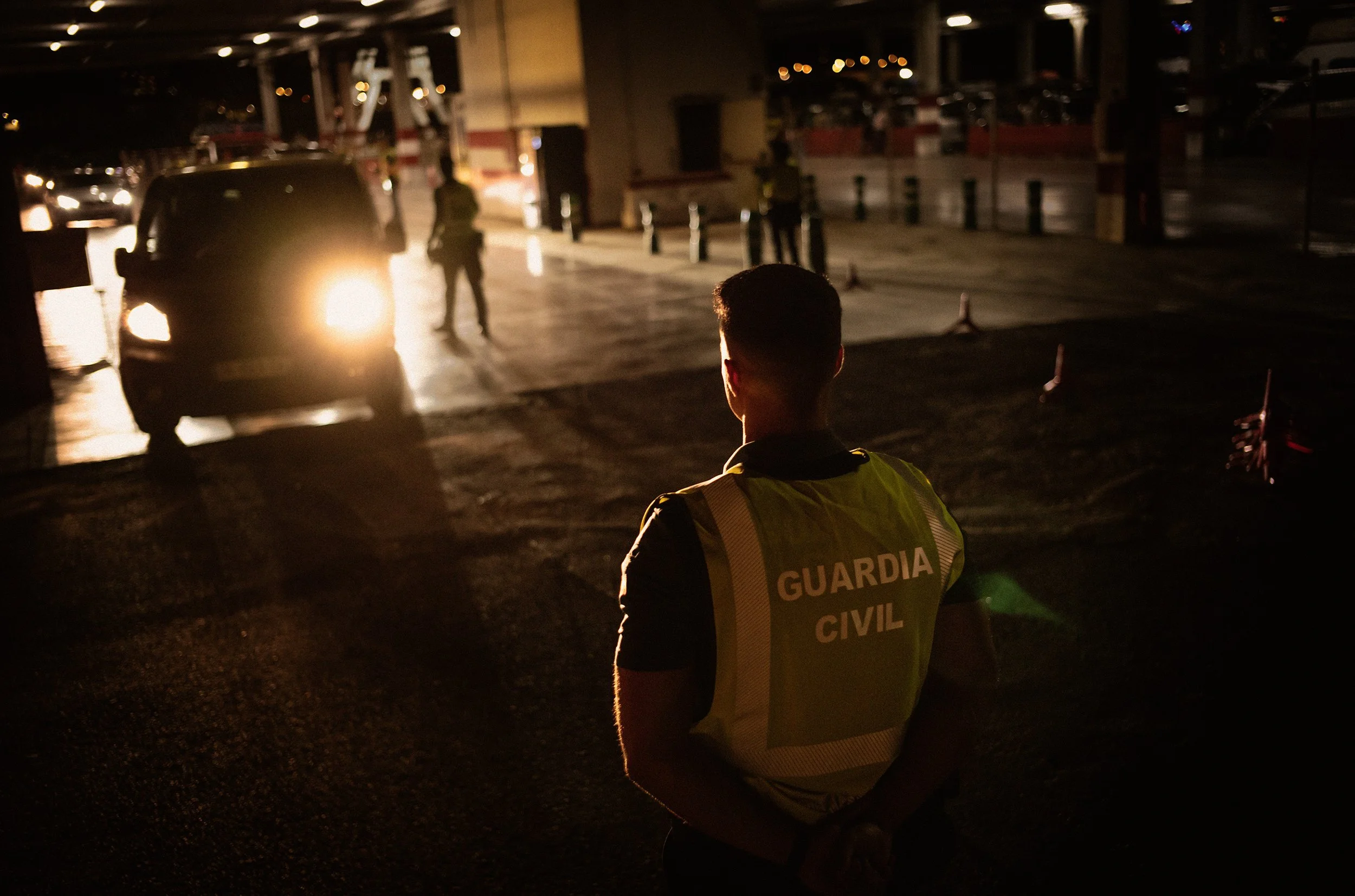 Agente de la Guardia Civil en la calle de noche, con luz de coche al fondo.