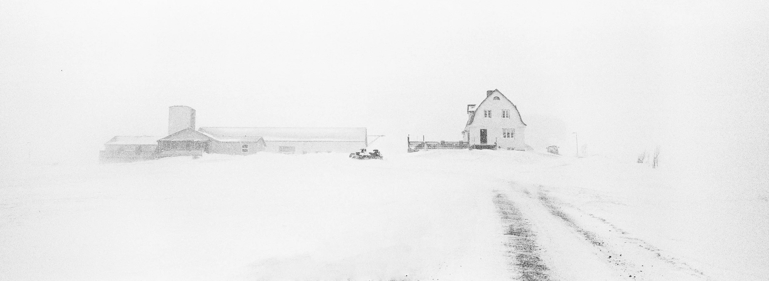 Casas y edificios en un paisaje nevado con camino de tierra cubierto de nieve y sin otras personas o animales visibles.