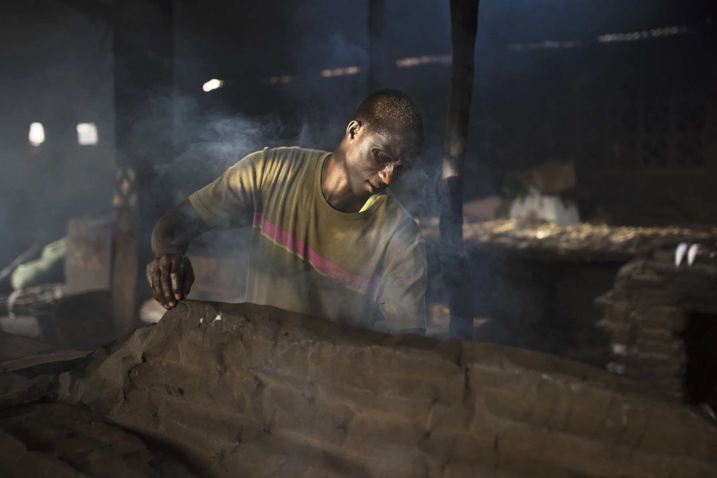 Hombre trabajando con barro en un entorno oscuro y fumoso.