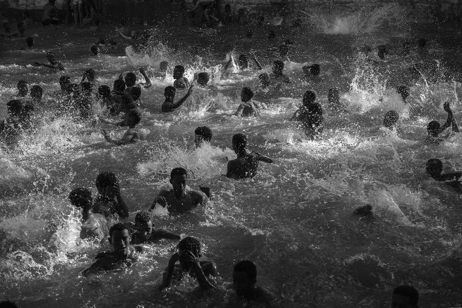 Muchos niños y adolescentes en un cuerpo de agua, nadando y jugando, en un entorno natural.