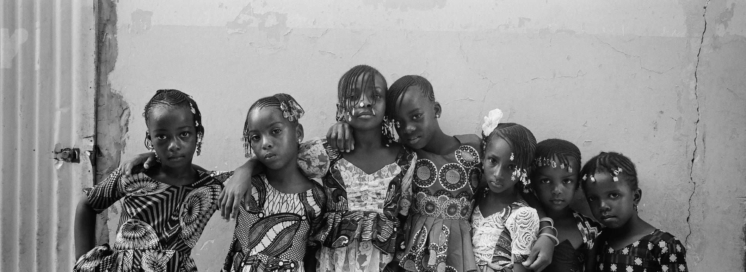 Grupo de niñas africanas con peinados y accesorios, posando juntas frente a una pared con grietas.