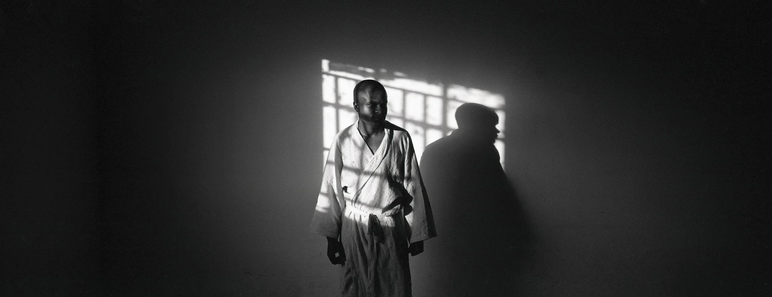 Persona de espaldas en una habitación oscura, luz de una ventana proyectando sombras en la pared.
