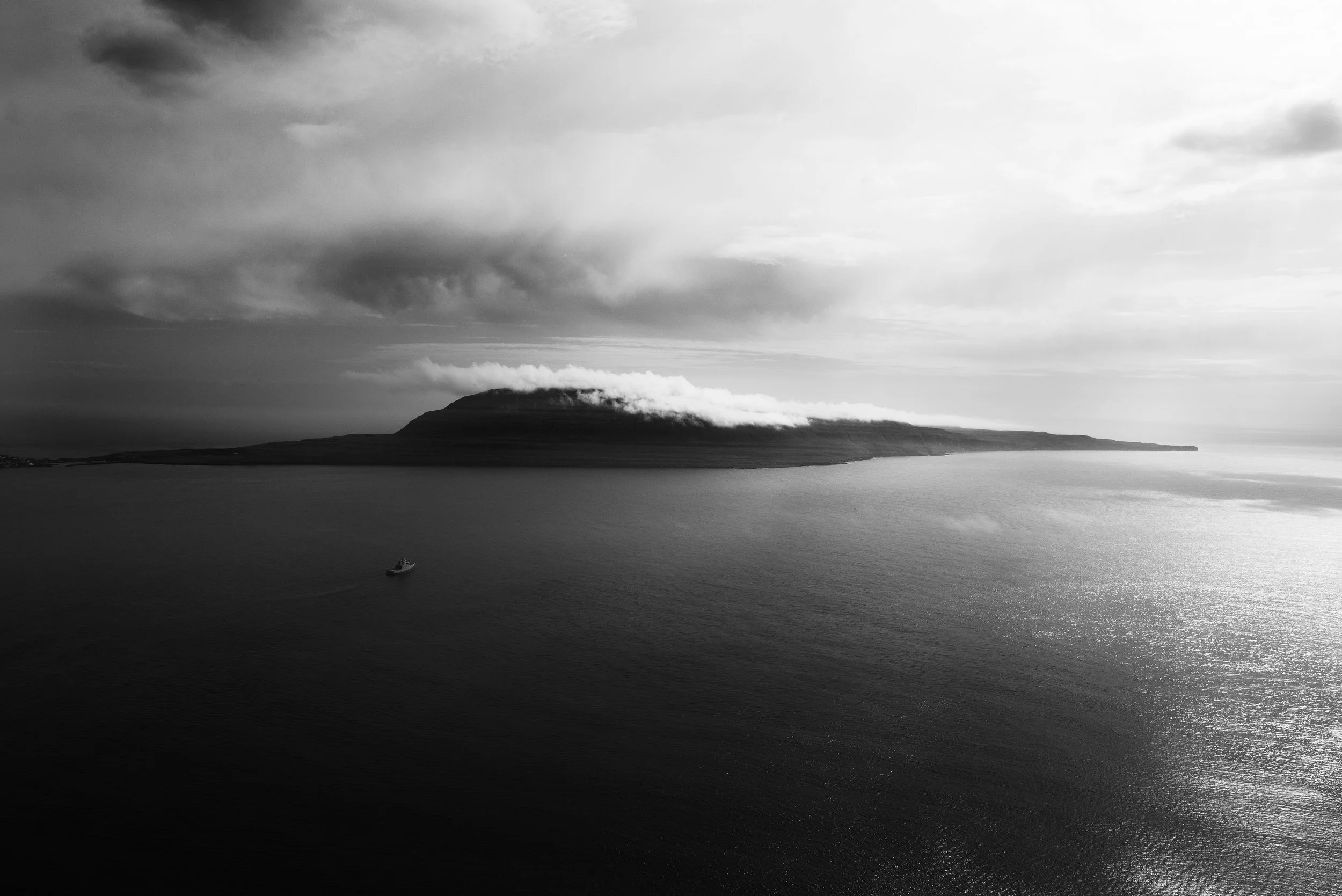 Una vista en blanco y negro de una isla con una colina en el centro, rodeada por agua, con un bote en el océano.