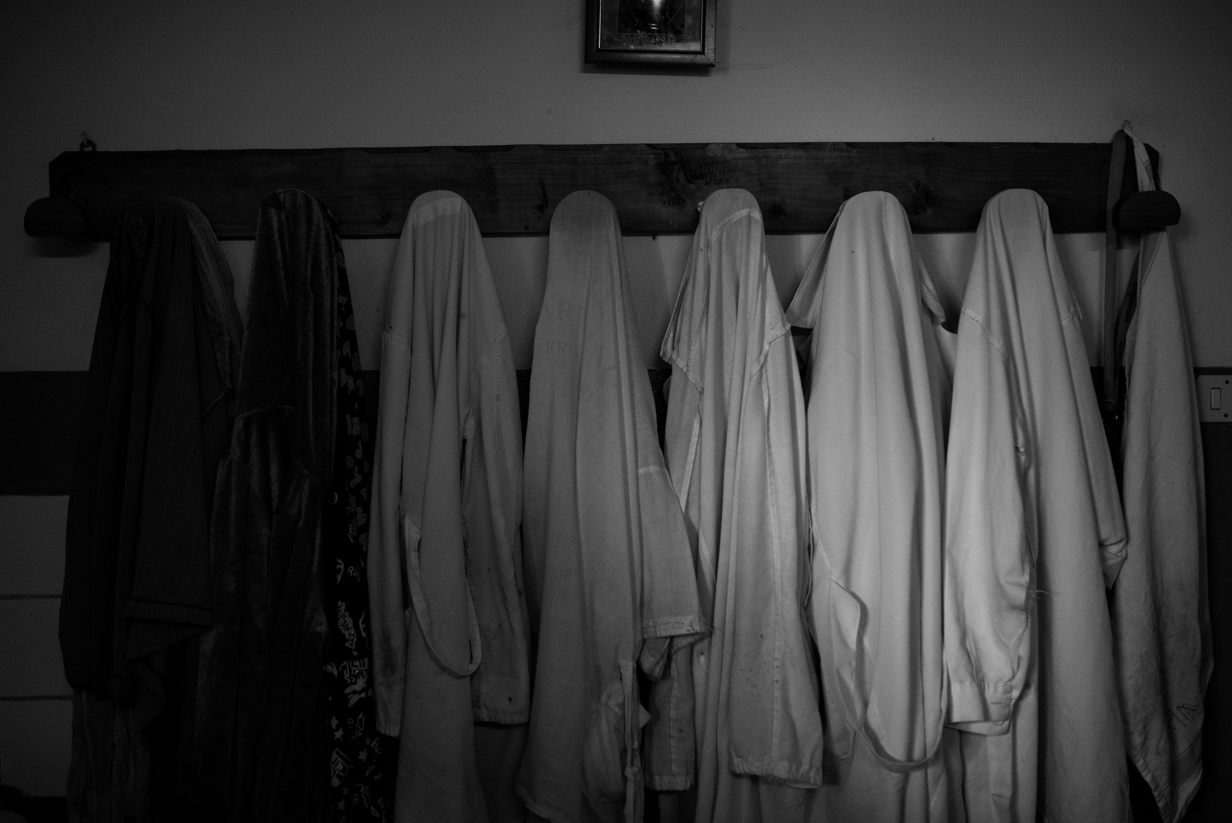 Ropa colgada en percha de madera sobre una pared, en tonos blancos y obscuros.