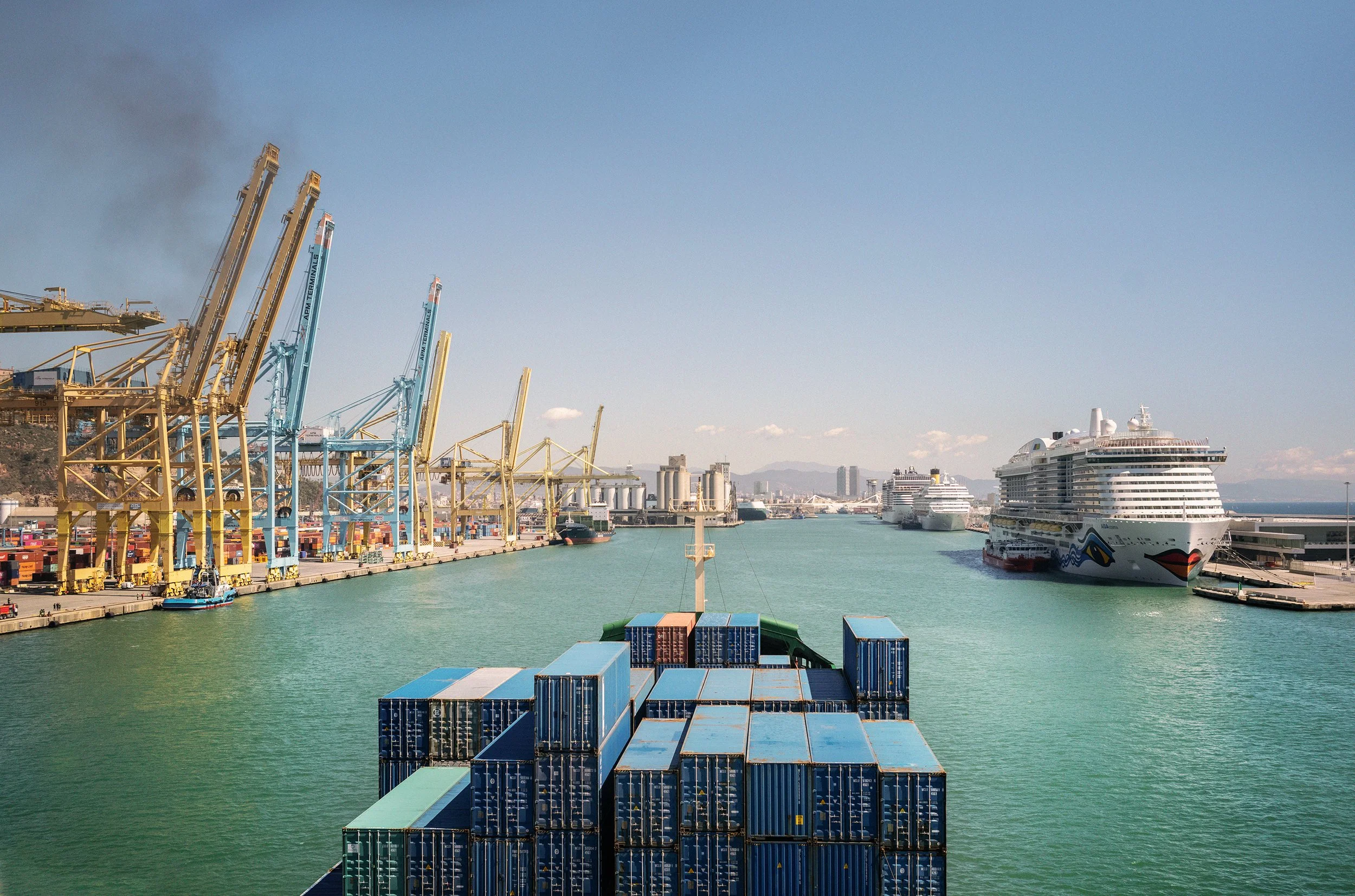 Vista del puerto con contenedores apilados, barcos de crucero y grúas industriales