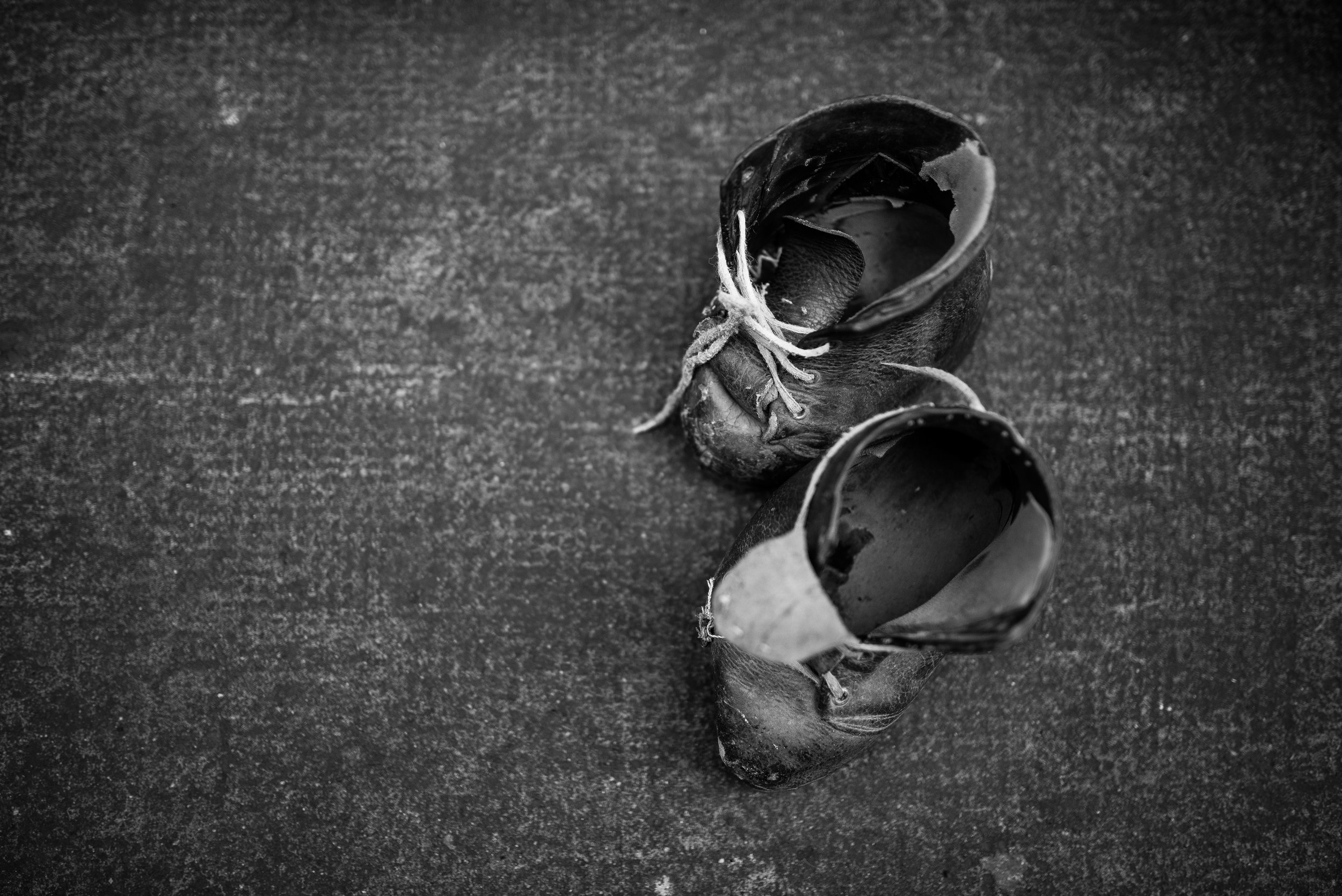 Un par de zapatos de charol negro viejos y desgastados en una superficie oscura y rugosa.