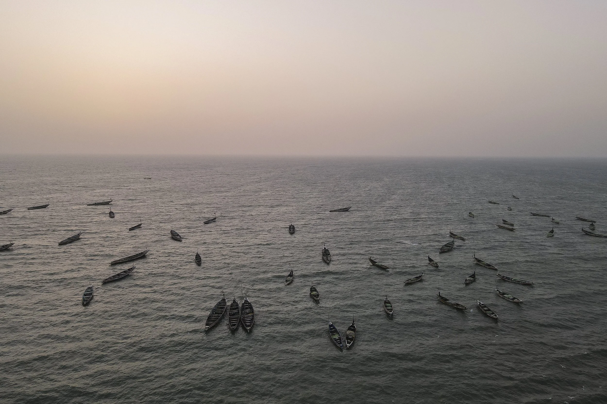 Vista aérea de varias embarcaciones en el mar al atardecer o amanecer, con cielo nublado y sin gente visible.