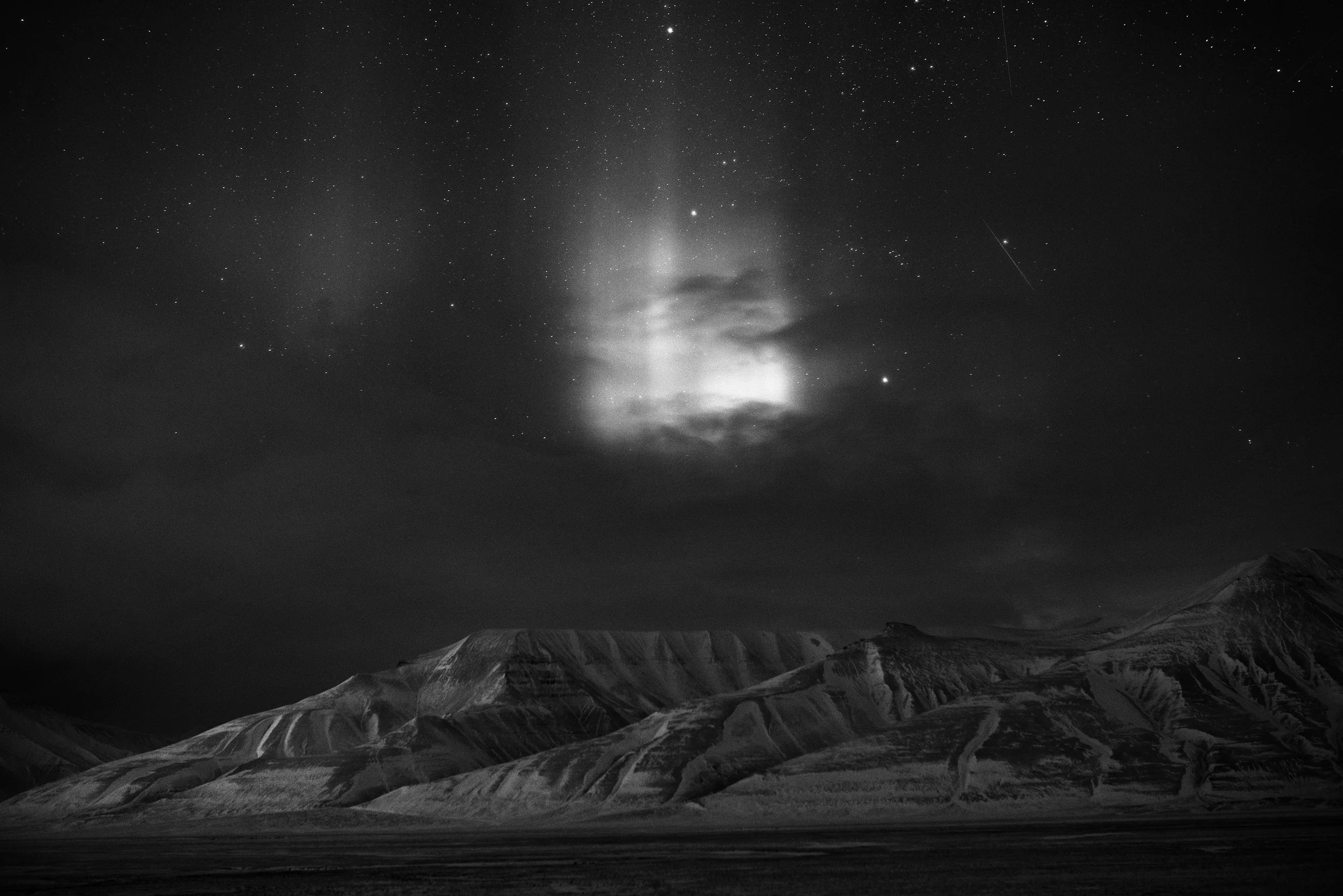 Montañas en primer plano y cielo estrellado con nubes y meteoros en segundo plano en una noche
