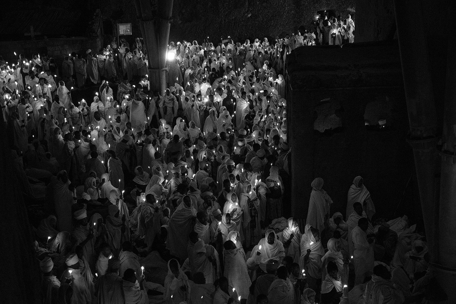 Muchísima gente vestida con túnicas blancas sosteniendo velas encendidas, participando en una ceremonia nocturna.