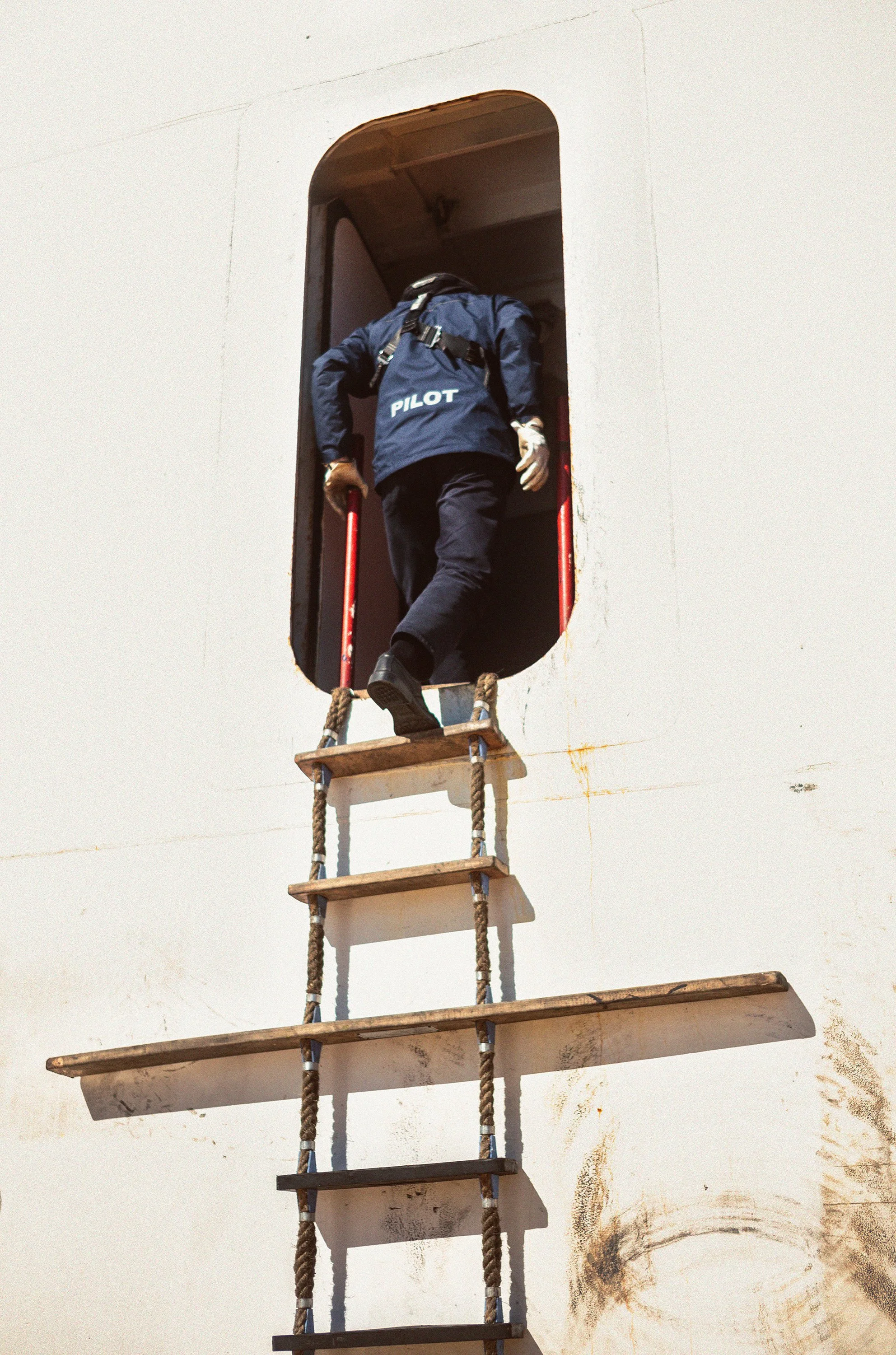 Persona con uniforme de piloto sube una escalera de madera y cuerda hacia la salida de un avión.