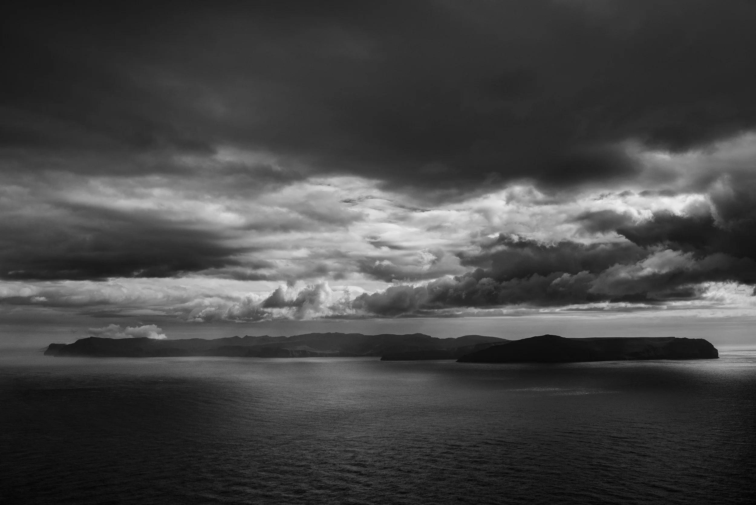 Paisaje marítimo con islas en el horizonte y un cielo nublado en tonos de gris.
