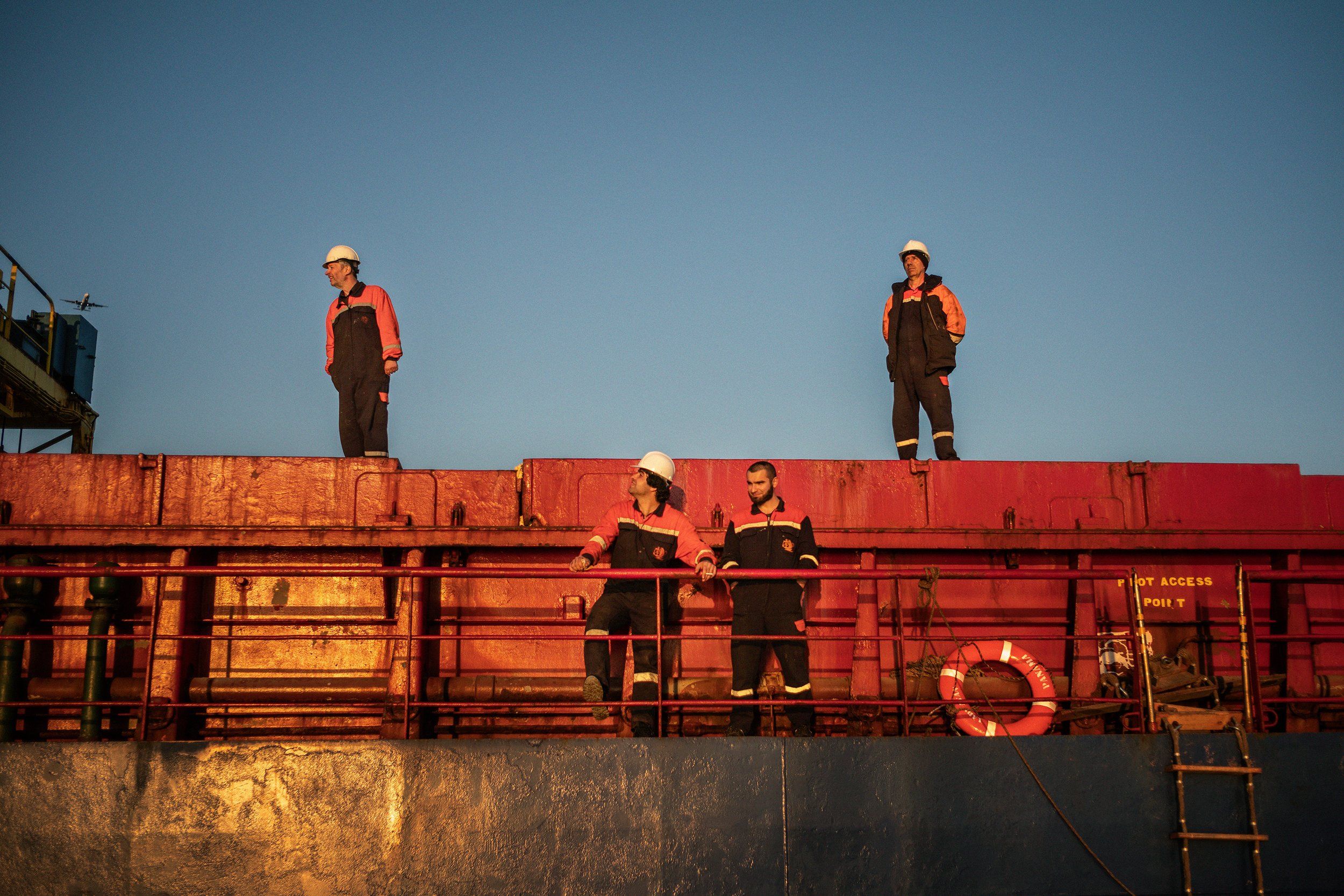 Cinco hombres con uniforme de trabajo y cascos de seguridad en una estructura metálica, con un cielo claro de fondo.