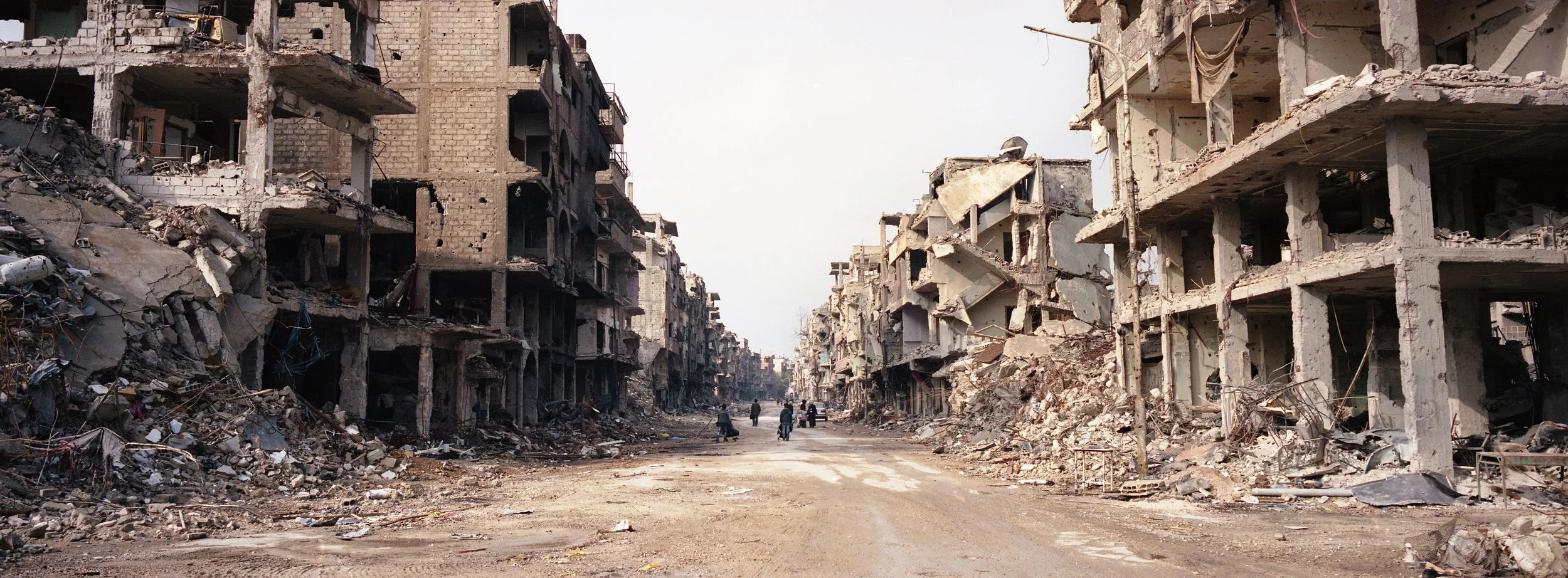 Edificios destruidos y ruinas en una calle abandonada, dejando un paisaje de destrucción y escombros.